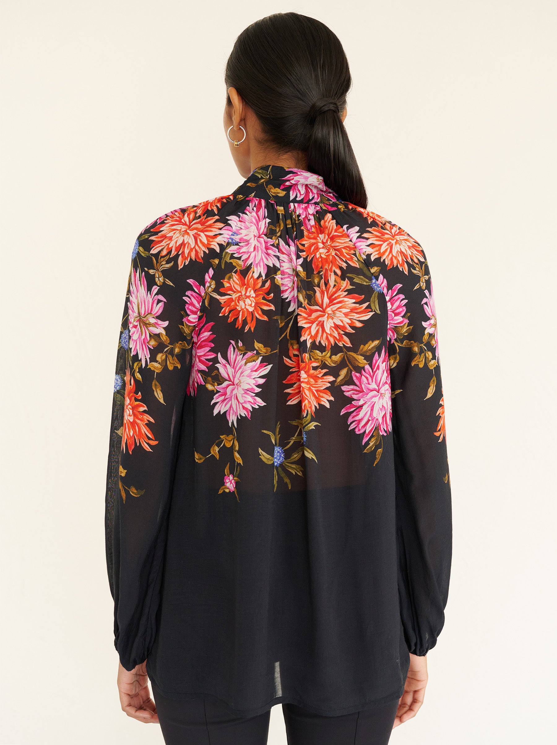 Back view close up of a model standing. She is wearing the Tara shirt in lightweight viscose voile with the Dahlia floral print. It is featuring a Victorian-style stand collar and fabric-covered buttons down the front.