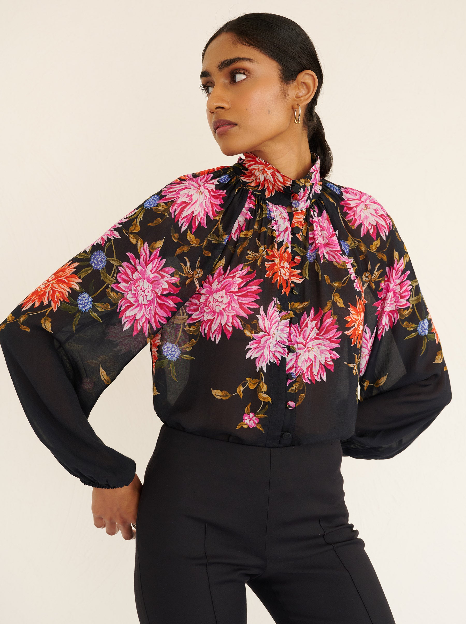 Front view close up of a model standing. She is wearing the Tara shirt in lightweight viscose voile with the Dahlia floral print. It is featuring a Victorian-style stand collar and fabric-covered buttons down the front.