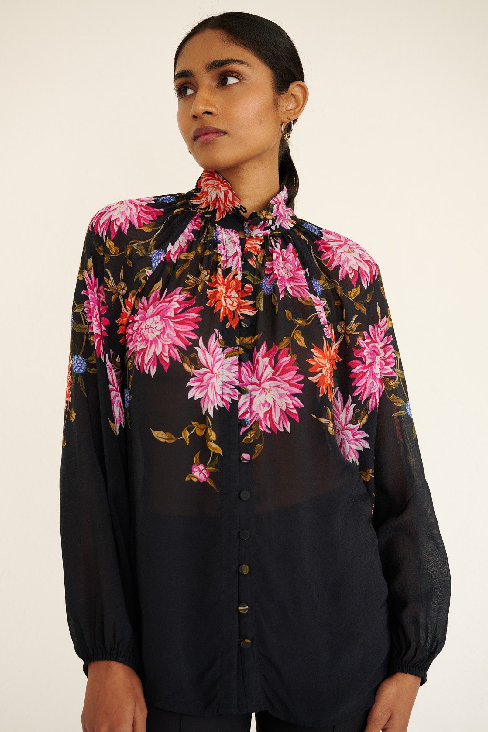 Front view close up of a model standing. She is wearing the Tara shirt in lightweight viscose voile with the Dahlia floral print. It is featuring a Victorian-style stand collar and fabric-covered buttons down the front.