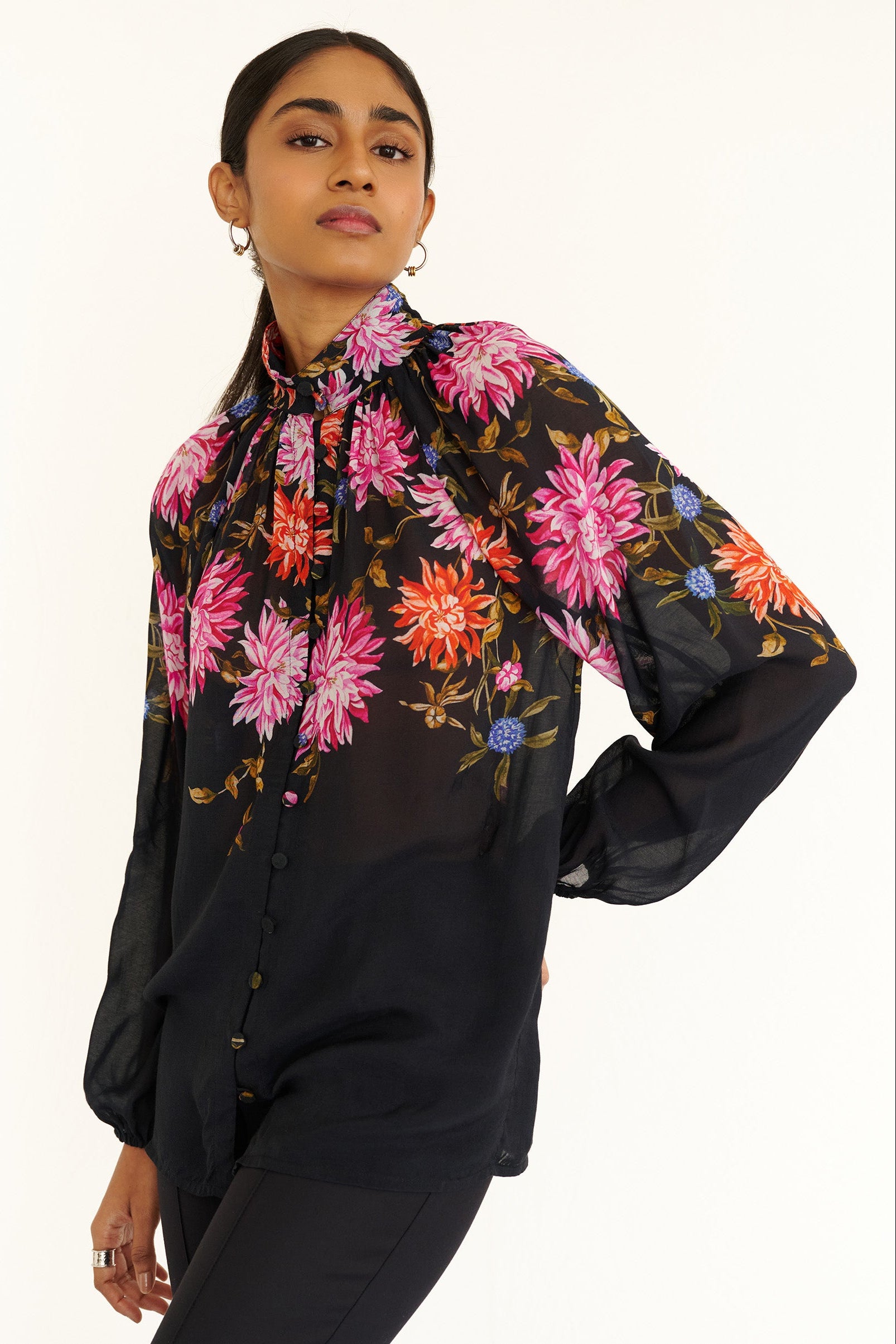 Front side view close up of a model standing. She is wearing the Tara shirt in lightweight viscose voile with the Dahlia floral print. It is featuring a Victorian-style stand collar and fabric-covered buttons down the front.