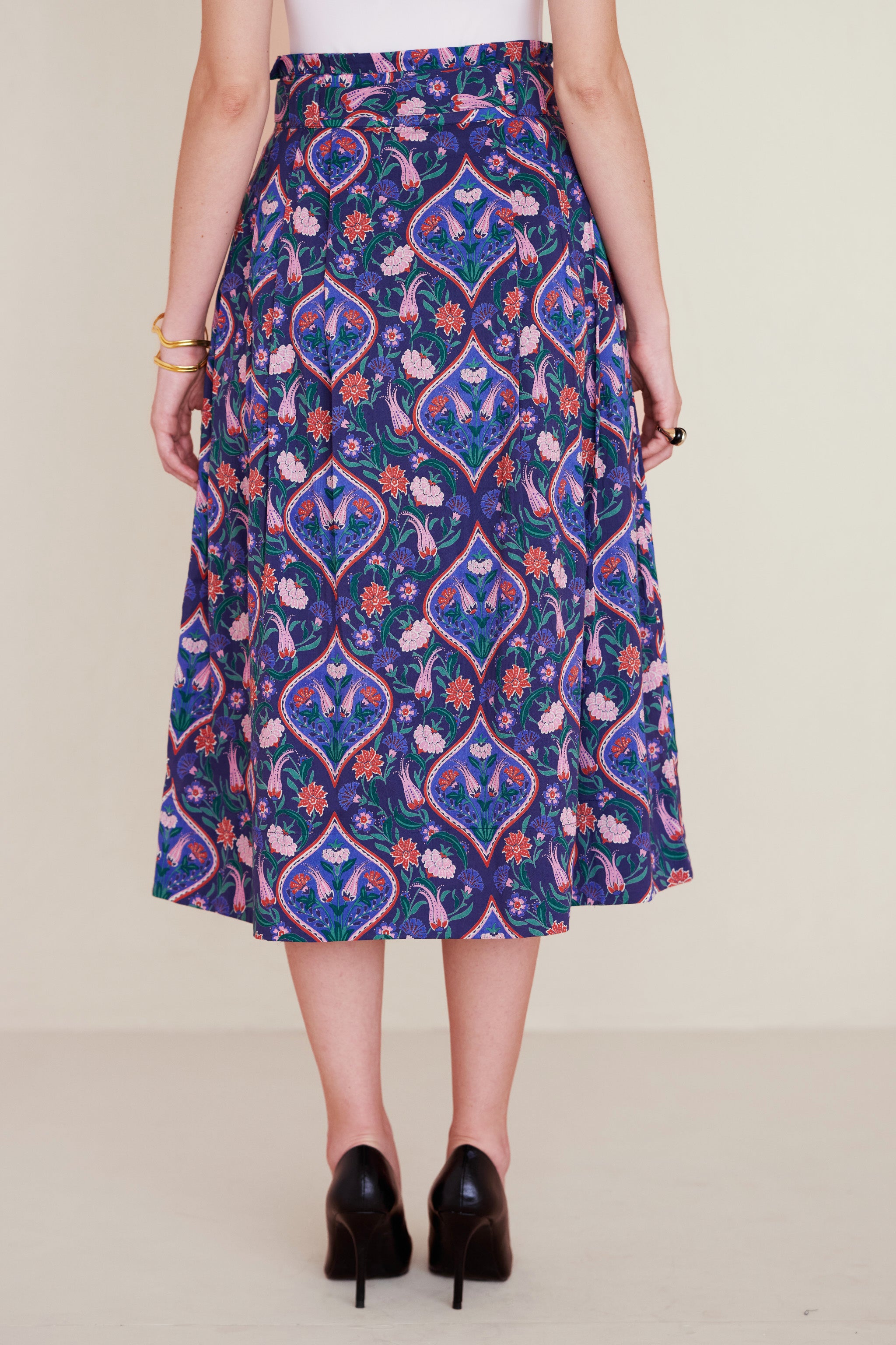Back view of woman wearing a midi skirt with a paperbag waist, fabric belt, and pockets, featuring a floral tile print inspired by decorative arts.