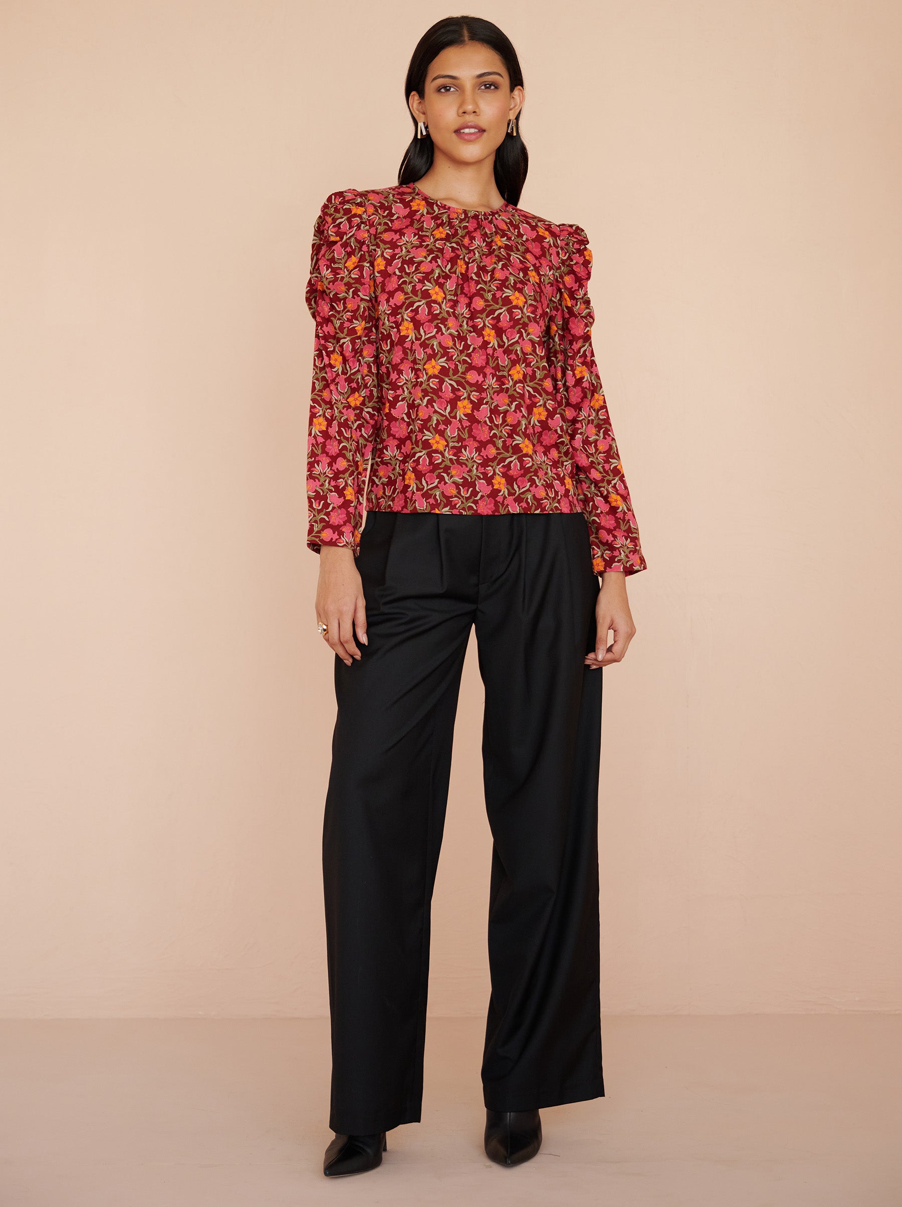 Front view of a model standing. She is wearing the Vincent top in eco-friendly viscose, featuring the Pomegranate Vine print in Azalea color. It has soft gathers at the neck and shoulders, long sleeves, and a crew neckline. The elegant day-to-night style fastens with a back zipper.