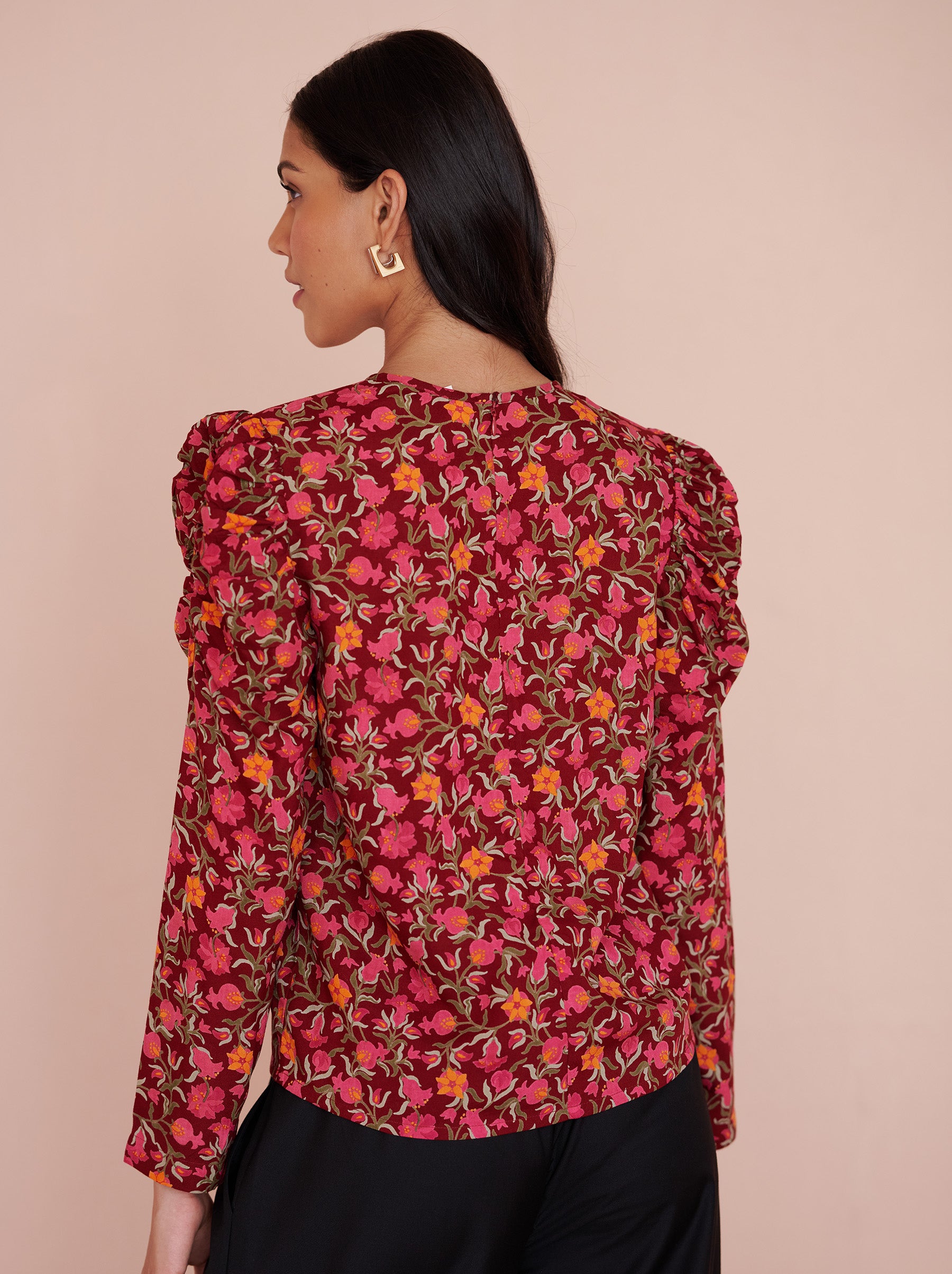 Back view close up of a model standing. She is wearing the Vincent top in eco-friendly viscose, featuring the Pomegranate Vine print in Azalea color. It has soft gathers at the neck and shoulders, long sleeves, and a crew neckline. The elegant day-to-night style fastens with a back zipper.