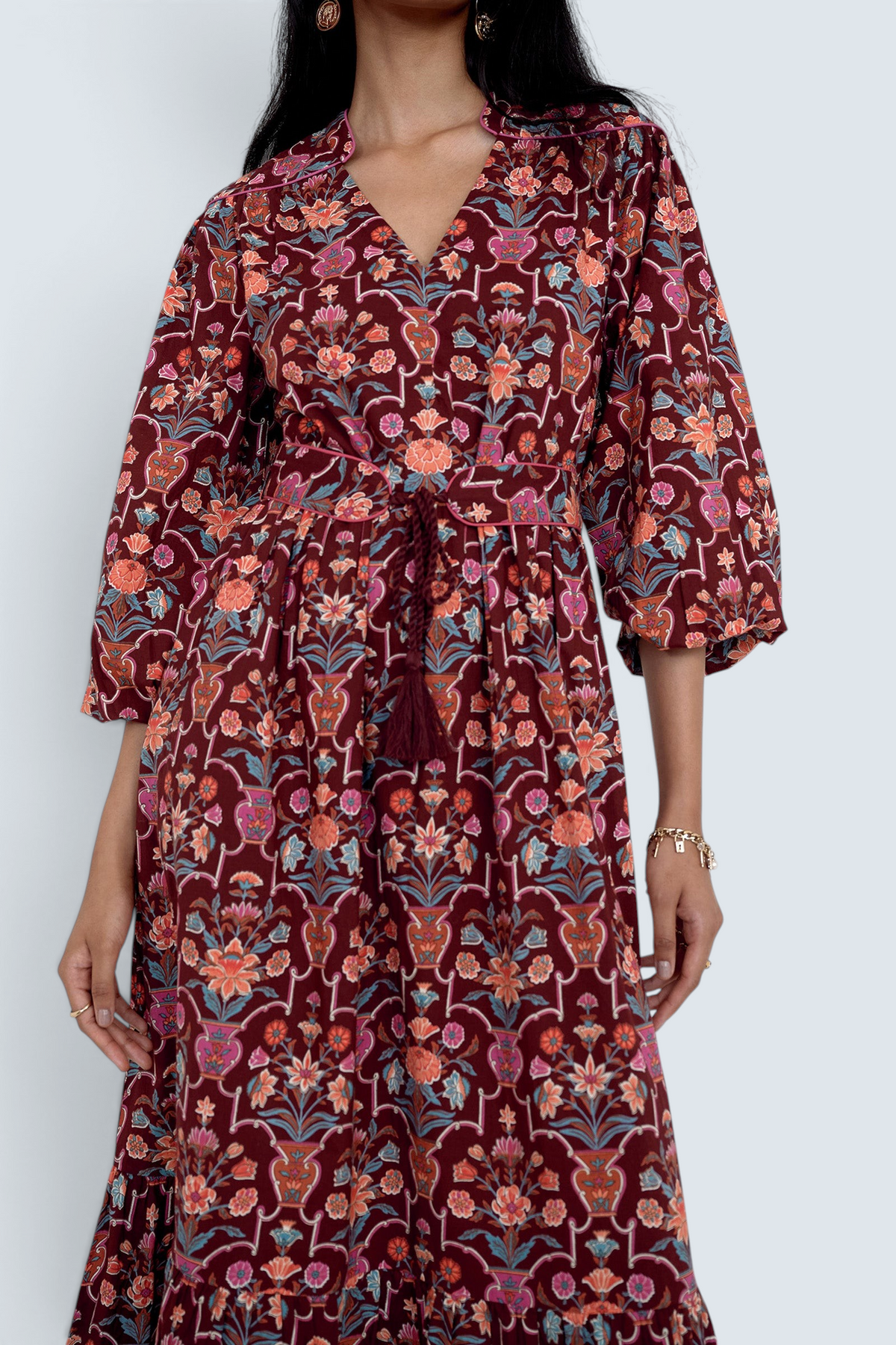 Front view close up of model standing wearing the Victoria dress in Floral Vase print. It features quilted shoulder details, piping, a tassel waist tie, and an easy silhouette.