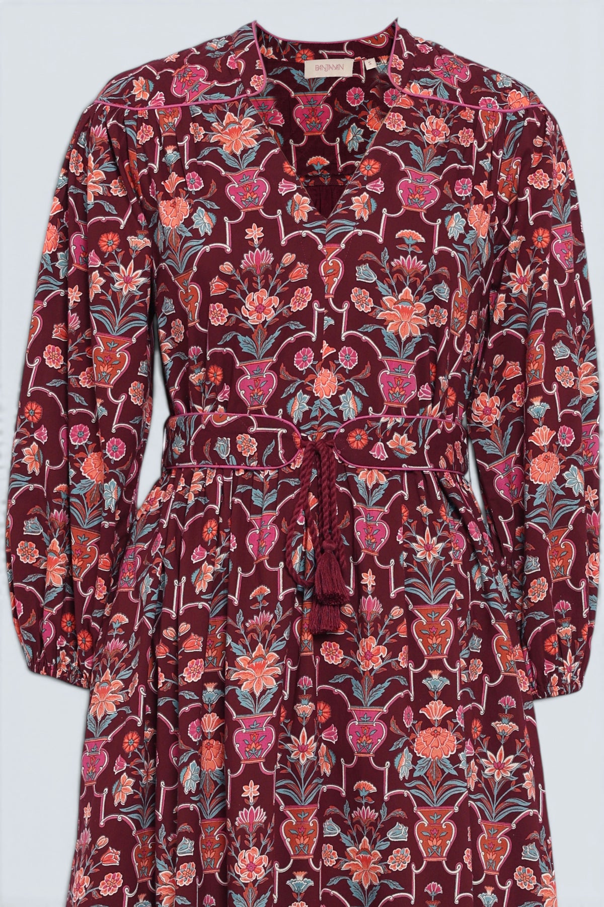 Front view close up of the Victoria dress in Floral Vase print. It features quilted shoulder details, piping, a tassel waist tie, and an easy silhouette.