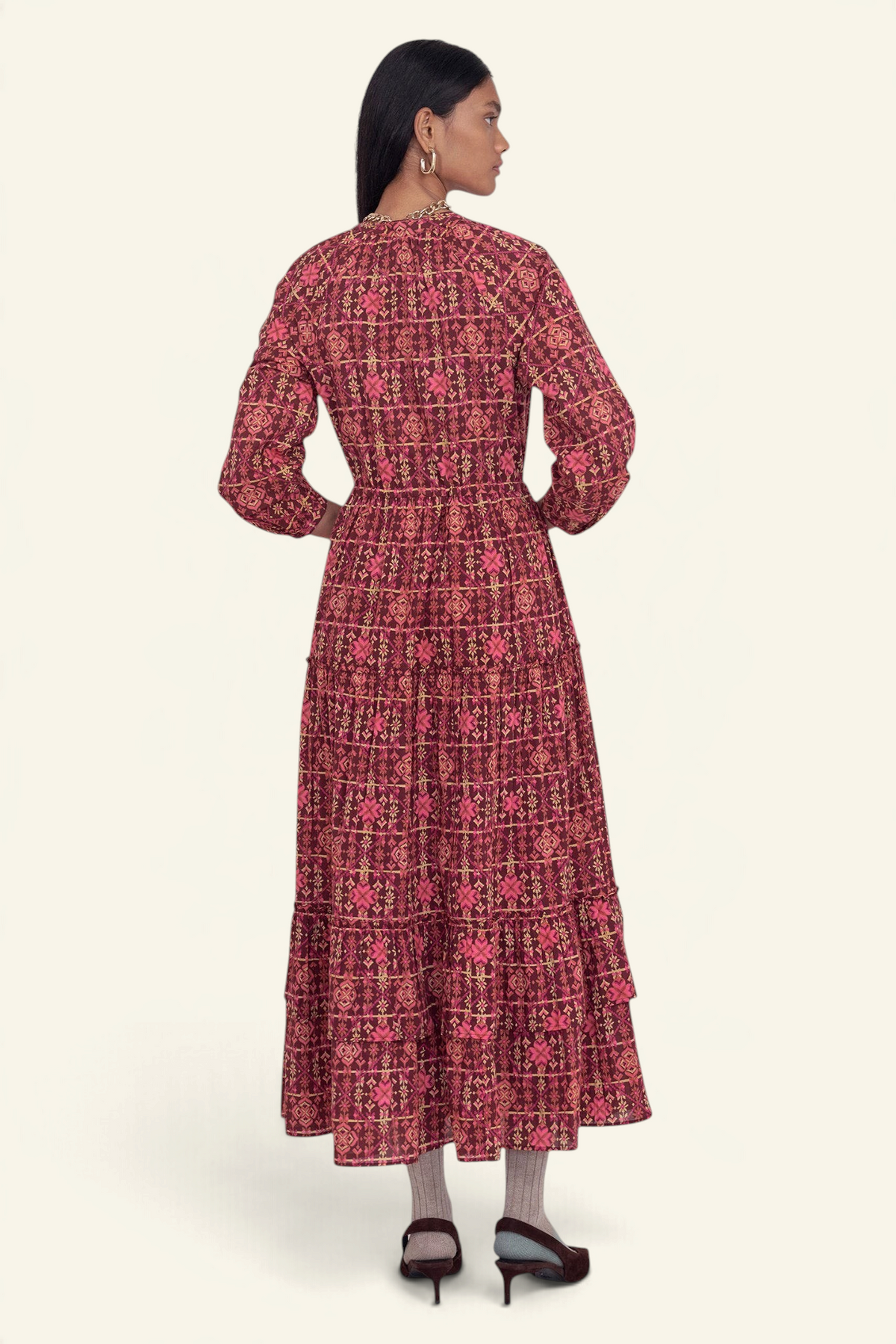 Back view of model standing wearing the Bazaar dress in Needlepoint print, featuring long sleeves, a tiered ankle-length A-line skirt, drawstring belt, and side-seam pockets.