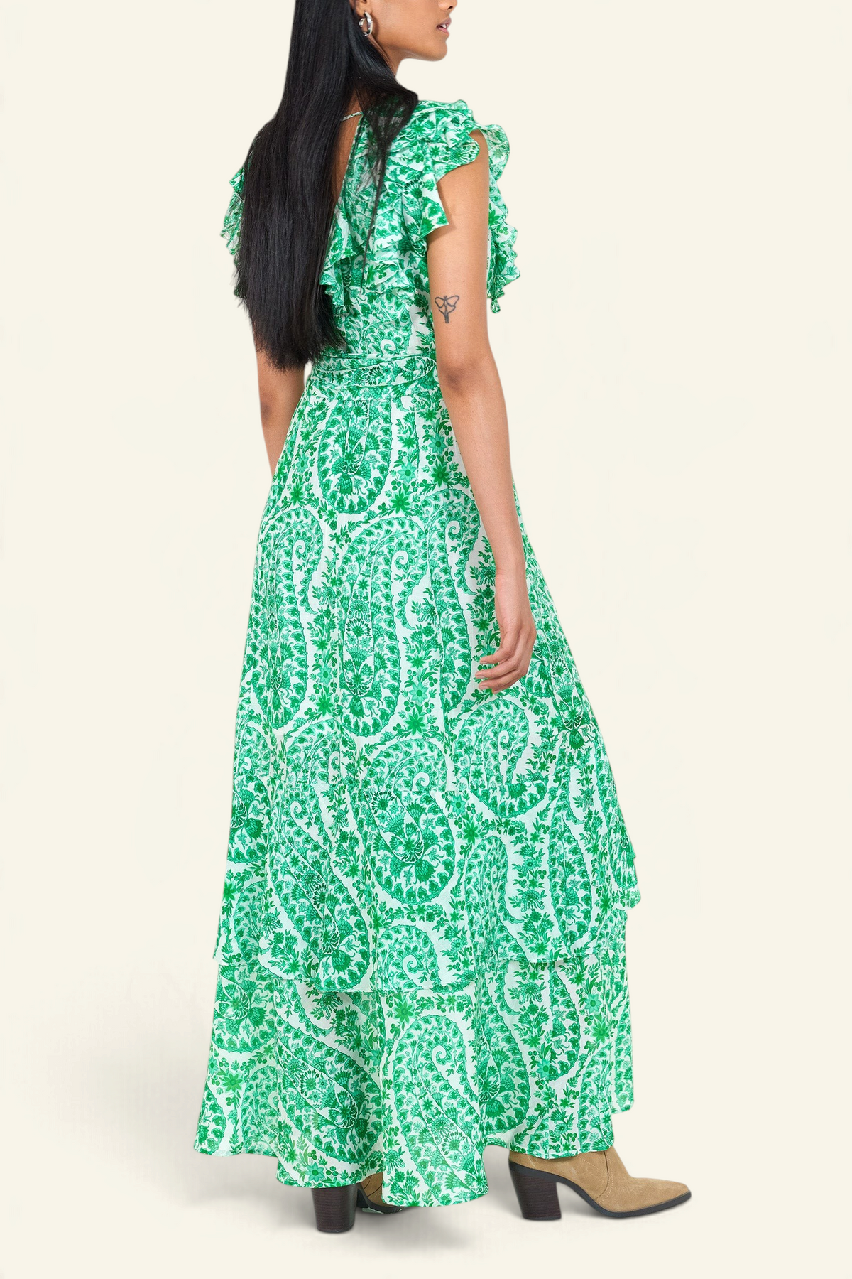 Side view of a woman standing. She is wearing the Beatrice dress in Paisley print, featuring a full-length tiered skirt, ruffled bodice, fabric tie belt, dramatic tie-back neckline, and lustrous cotton silk.