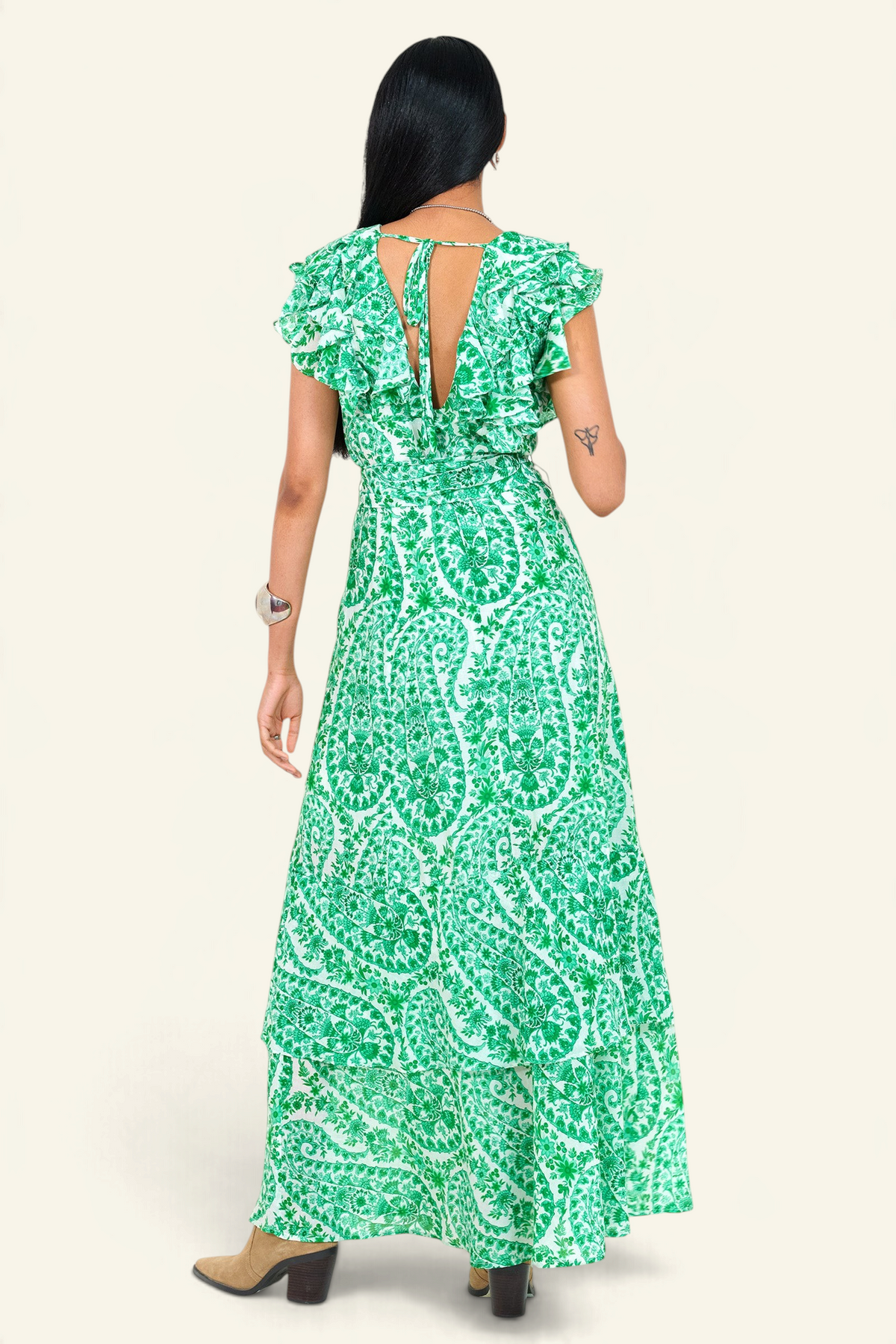 Back view of a woman standing. She is wearing the Beatrice dress in Paisley print, featuring a full-length tiered skirt, ruffled bodice, fabric tie belt, dramatic tie-back neckline, and lustrous cotton silk.