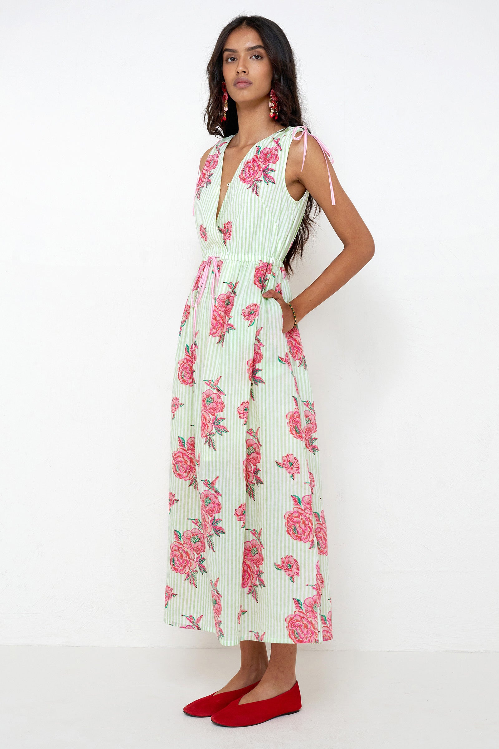 Side view of woman standing. She is wearing the Becca dress in the Eliza Rose print, featuring an adjustable waist, shoulder ties, a deep V-neckline, and hand block-printed floral motifs with hummingbird details.