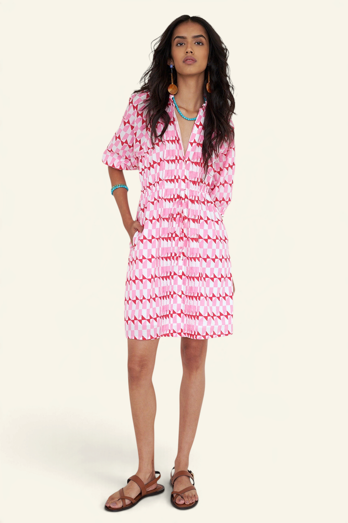 Front view of woman standing. She is wearing the Benita dress in the Stevie print, featuring a shirtdress silhouette, button-front placket, drawstring waist, and geometric motifs inspired by the French Riviera.