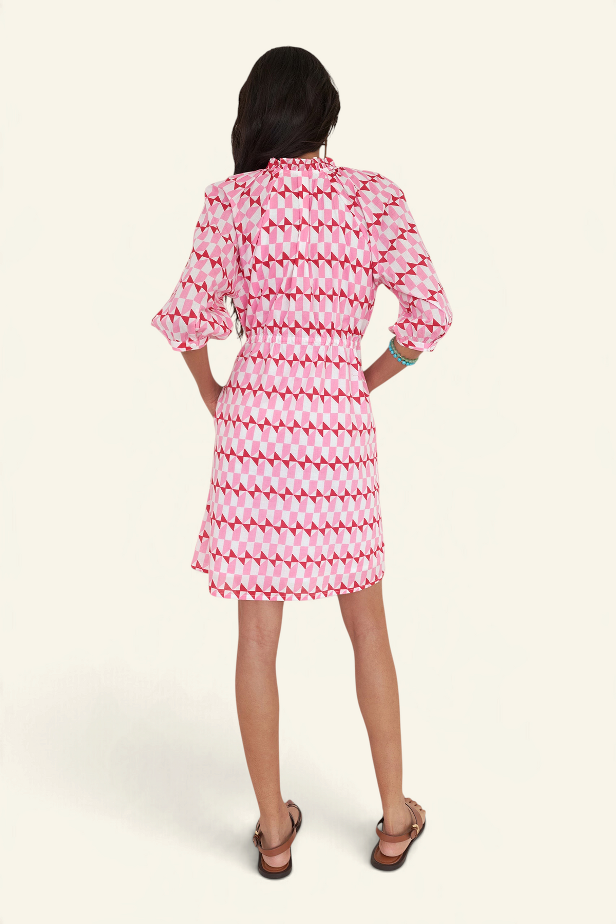 Back view of woman standing. She is wearing the Benita dress in the Stevie print, featuring a shirtdress silhouette, button-front placket, drawstring waist, and geometric motifs inspired by the French Riviera.