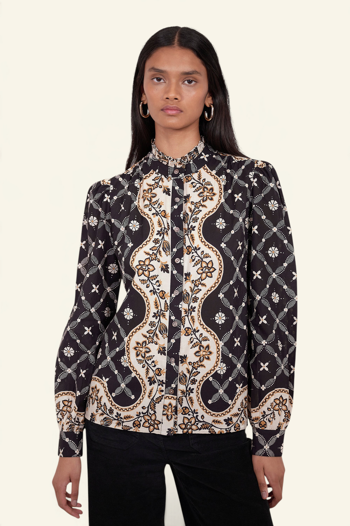 Front view of model standing. She is wearing Banjanan Christina shirt in black with a Victorian-inspired geometric bandana print, frilled collar, and puff sleeves.