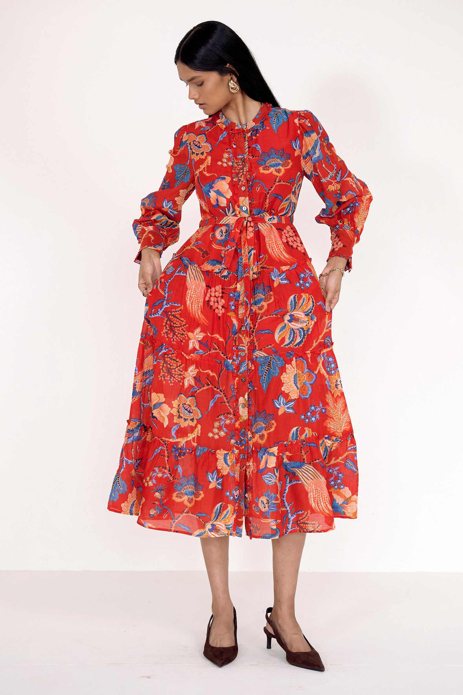 Front view of model standing. She is wearing the Emira dress in Chintz print. It features a flowing skirt, delicate ruffles, fabric-covered buttons, and a detachable belt.