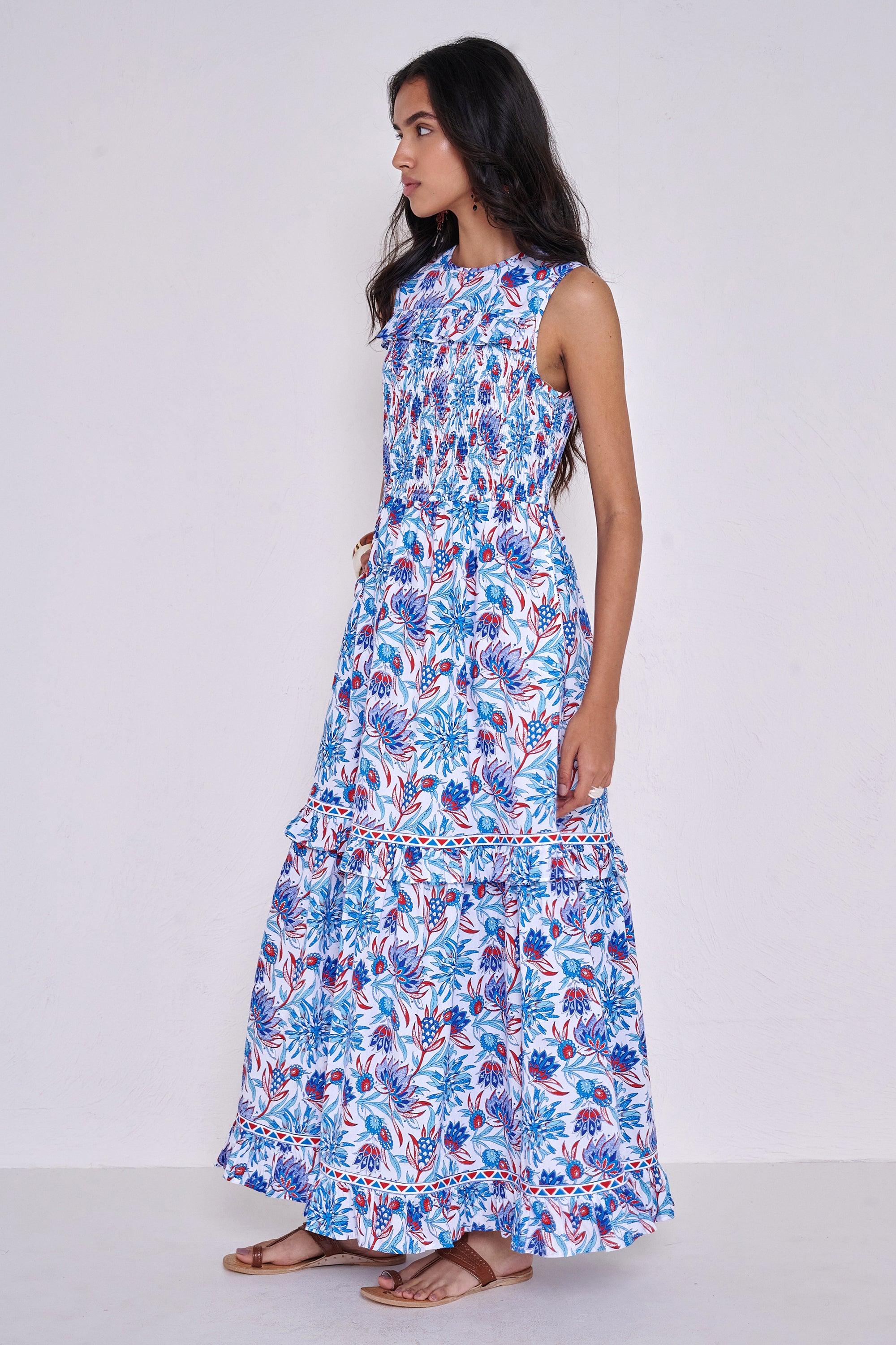 Side view close up of woman standing. She is wearing the Iris dress in the Philippa print, featuring a smocked bodice, A-line silhouette, and red, white, and blue floral motifs inspired by Provence’s wild thistles and vines.