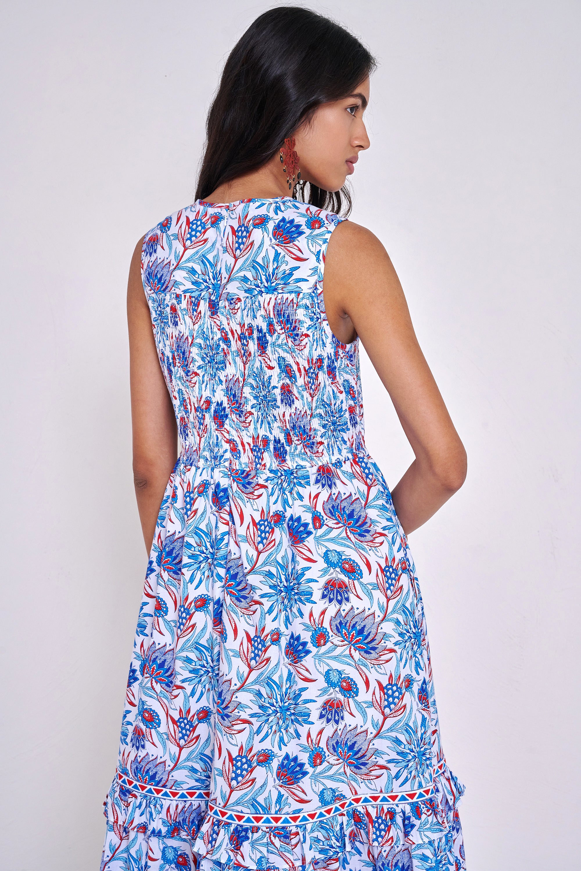 Back view close up of woman standing. She is wearing the Iris dress in the Philippa print, featuring a smocked bodice, A-line silhouette, and red, white, and blue floral motifs inspired by Provence’s wild thistles and vines.