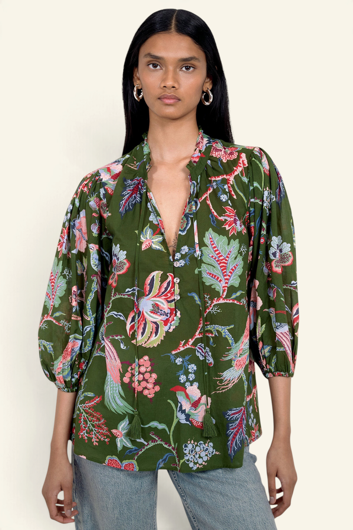 Front view of model standing. She is wearing the Lorna top in Chintz print, featuring a V-neck with a soft ruffle and tie, a loose flowing body, and slightly voluminous sleeves, paired with jeans.
