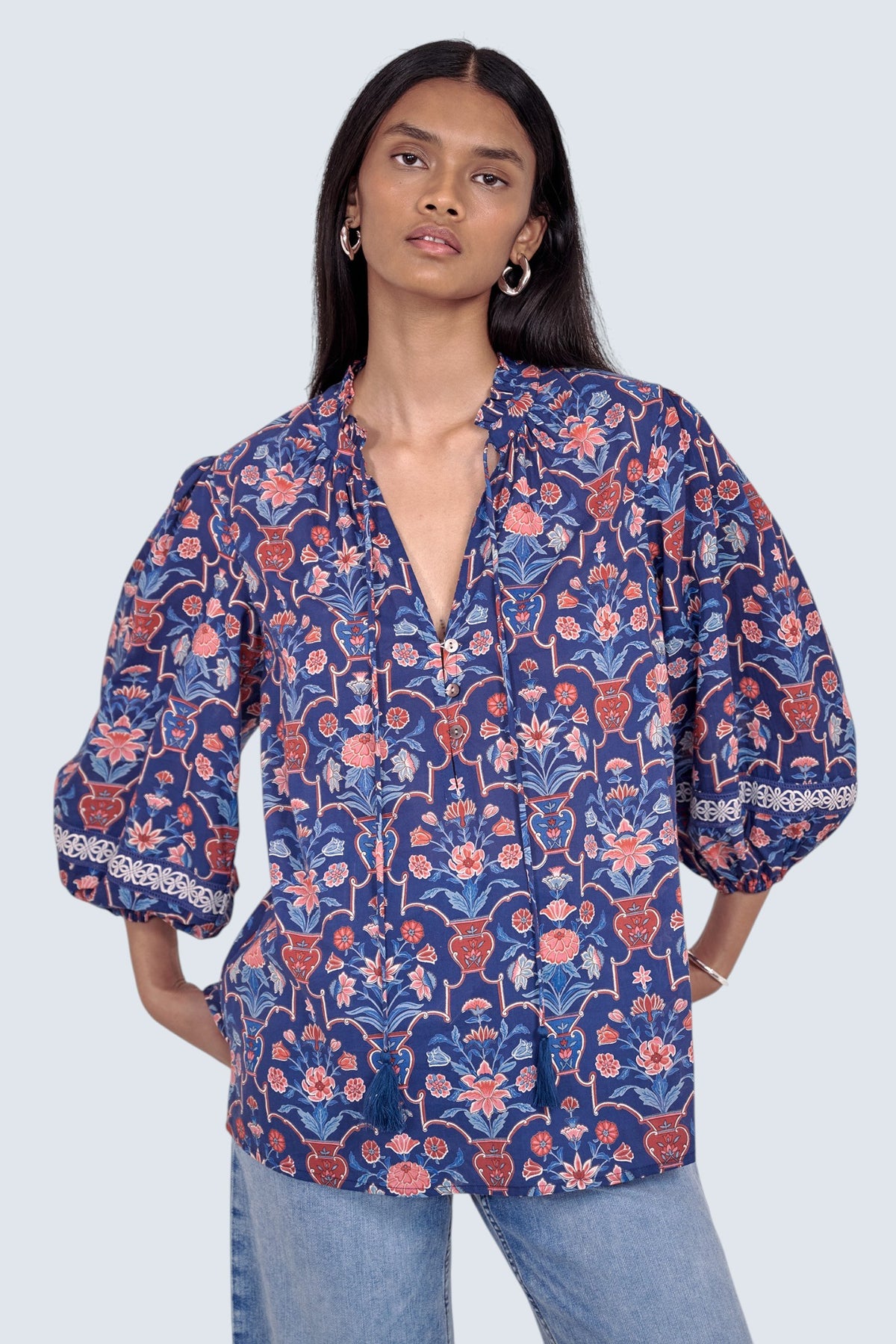 Front view of model standing wearing the Lorna top in Floral Vase print, featuring a V-neck with ruffle and tie, lace-trimmed sleeves, and a loose flowing silhouette, paired with jeans.