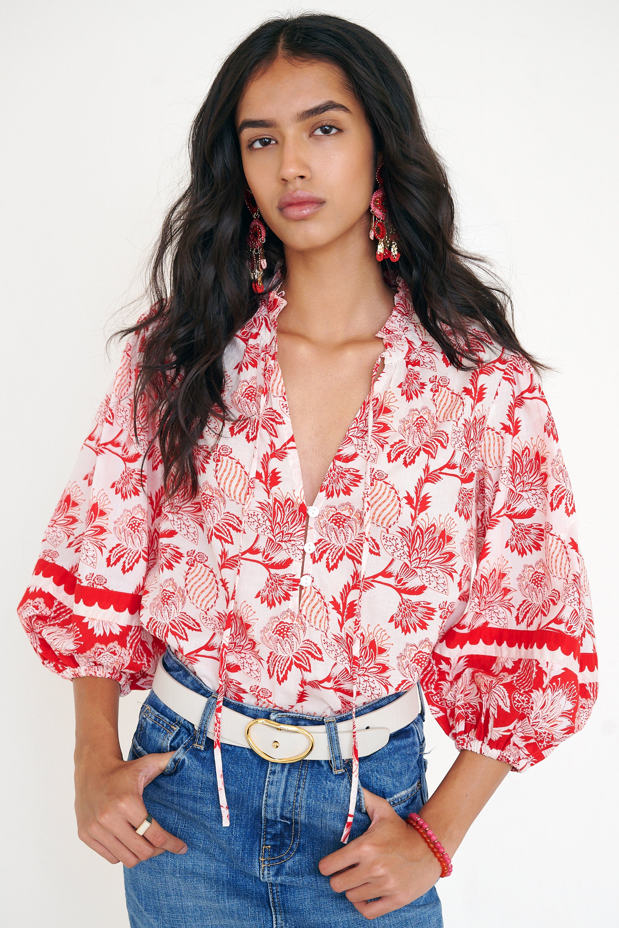 Front view of woman standing. She is wearing the Lorna top in the Lizzie print, featuring a V-neck with a soft ruffle, adjustable tie closure, voluminous sleeves, and winding floral vine motifs.