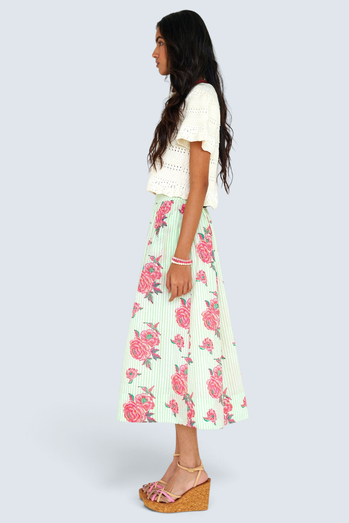 Side view of woman standing wearing the Magdalena skirt in the Eliza Rose print, featuring all-around pleats & hand block-printed floral motifs.