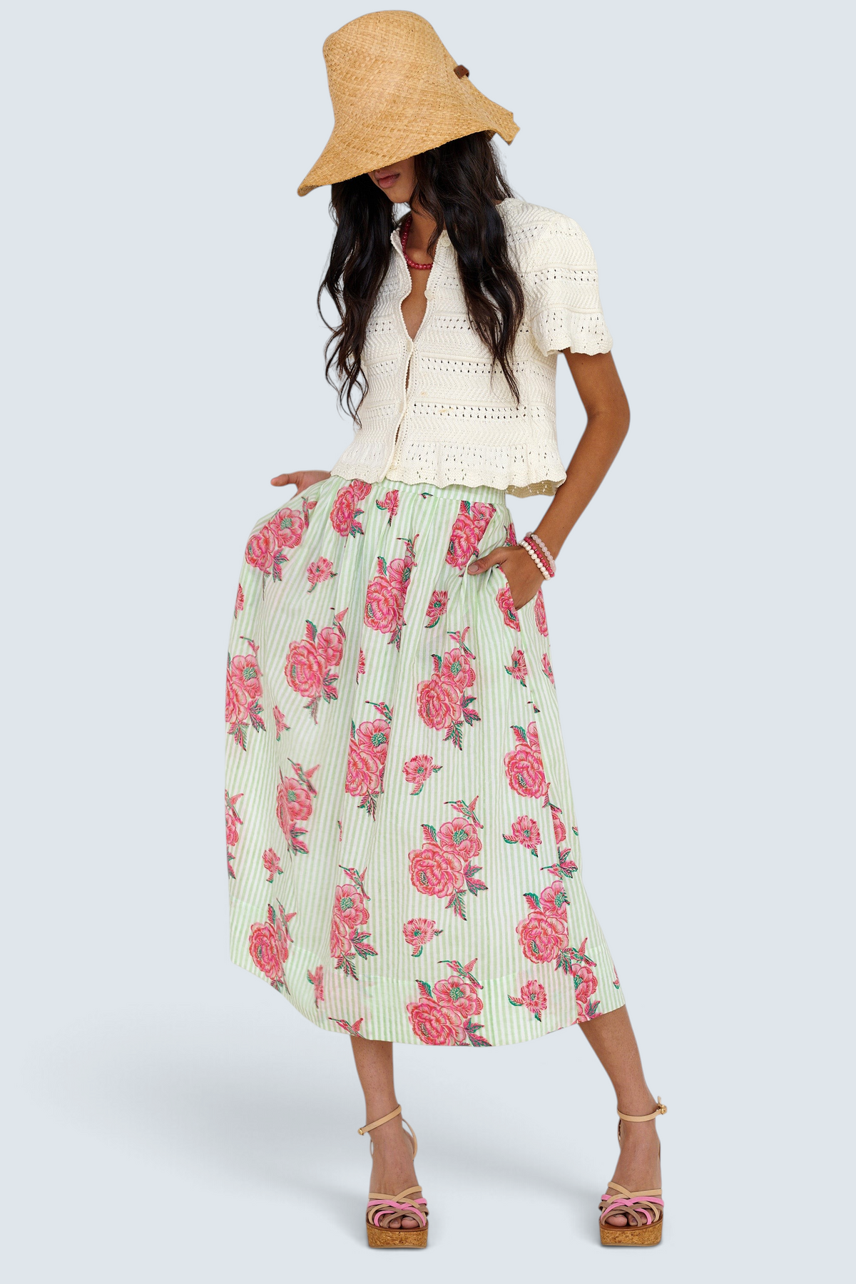 Front view of woman standing wearing the Magdalena skirt in the Eliza Rose print, featuring all-around pleats & hand block-printed floral motifs. Paired with laura crochet cardigan in ivory.