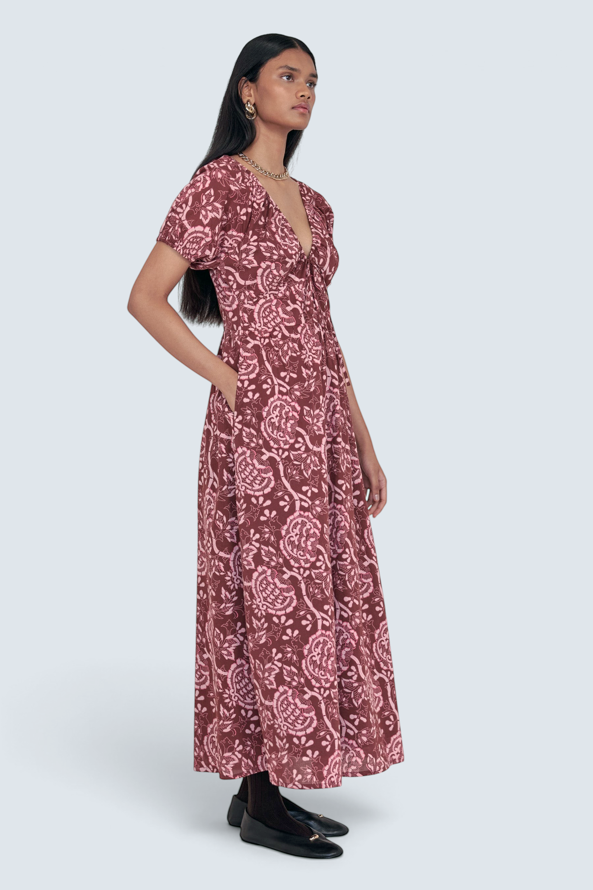 Side view of model standing. She is wearing the Norma dress in Coromandel print, featuring a drawstring neckline, elasticated sleeves, a flattering princess seam waist, and side-seam pockets.