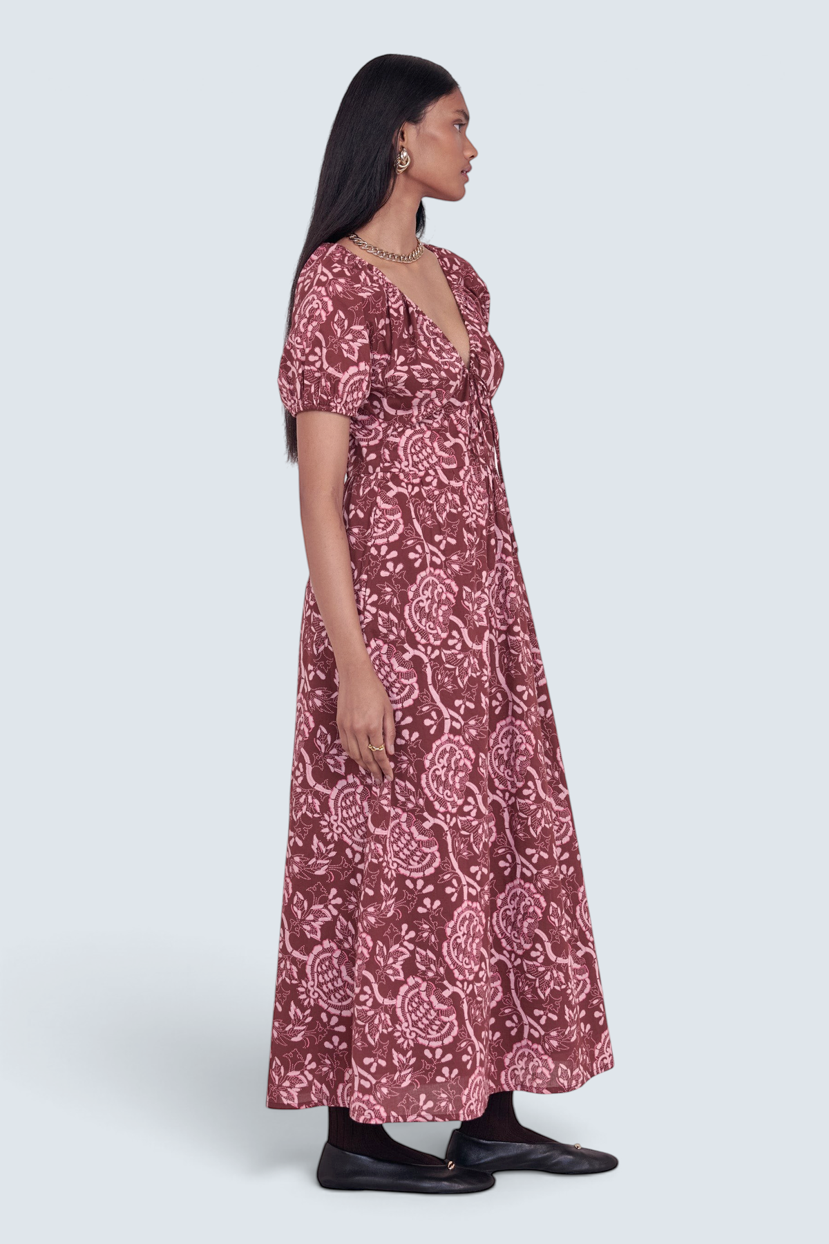 Side view of model standing. She is wearing the Norma dress in Coromandel print, featuring a drawstring neckline, elasticated sleeves, a flattering princess seam waist, and side-seam pockets.