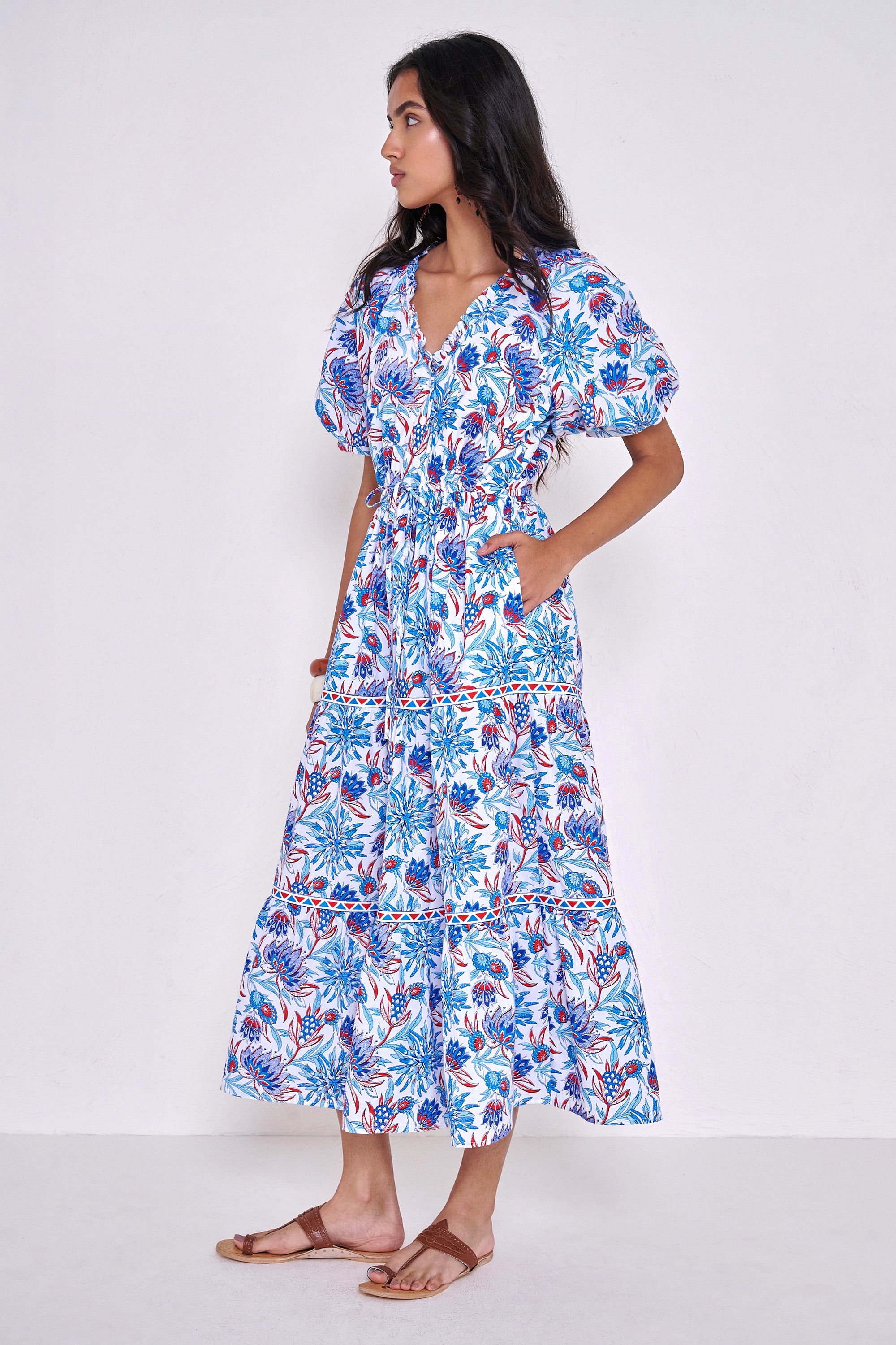 Side view of woman standing wearing the Poppy dress in the Philippa print, featuring raglan blouson sleeves, a button-front placket, a flowing skirt, and floral motifs inspired by the wildflowers of Provence.