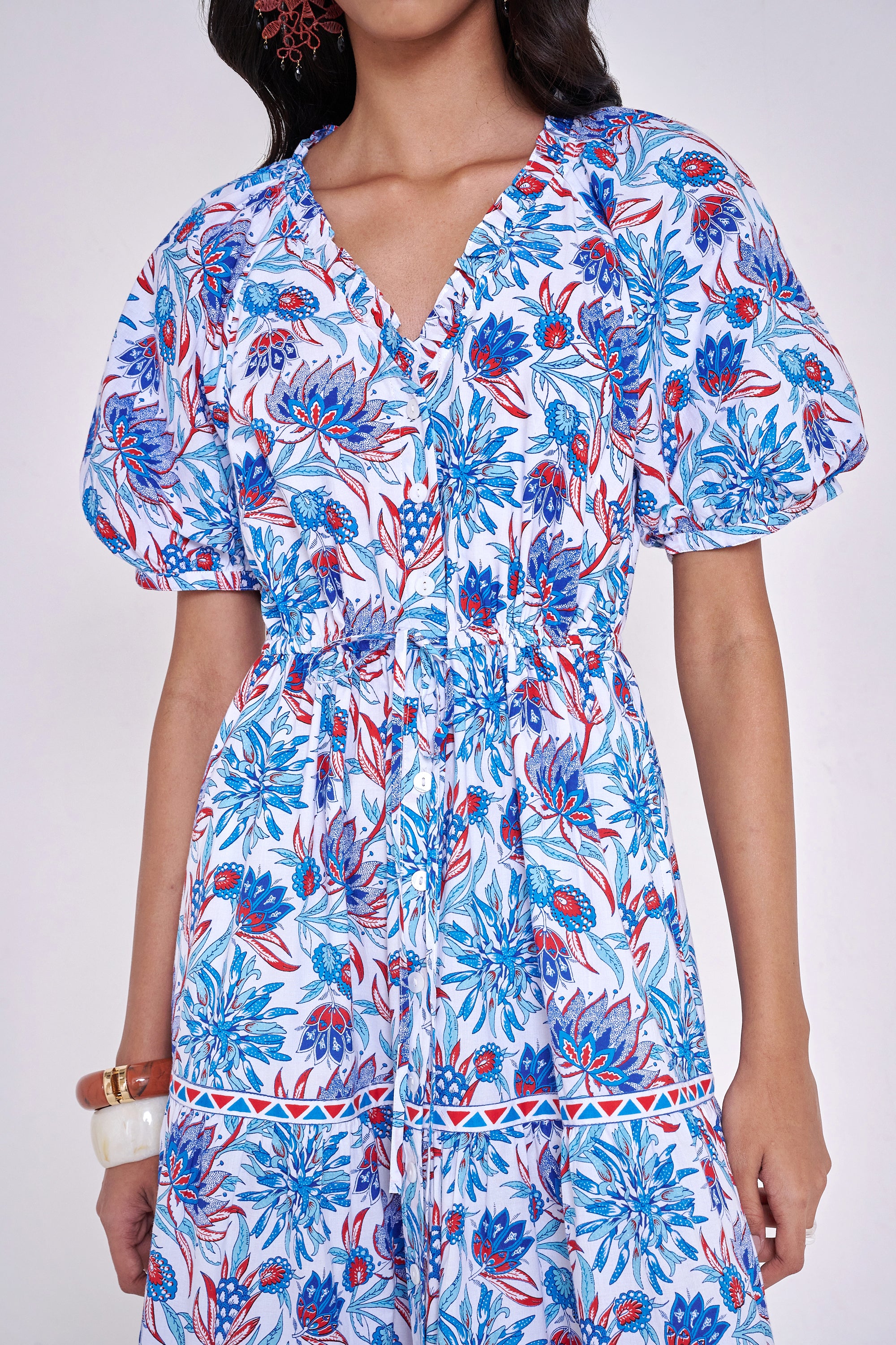Front view close up of woman standing wearing the Poppy dress in the Philippa print, featuring raglan blouson sleeves, a button-front placket, a flowing skirt, and floral motifs inspired by the wildflowers of Provence.