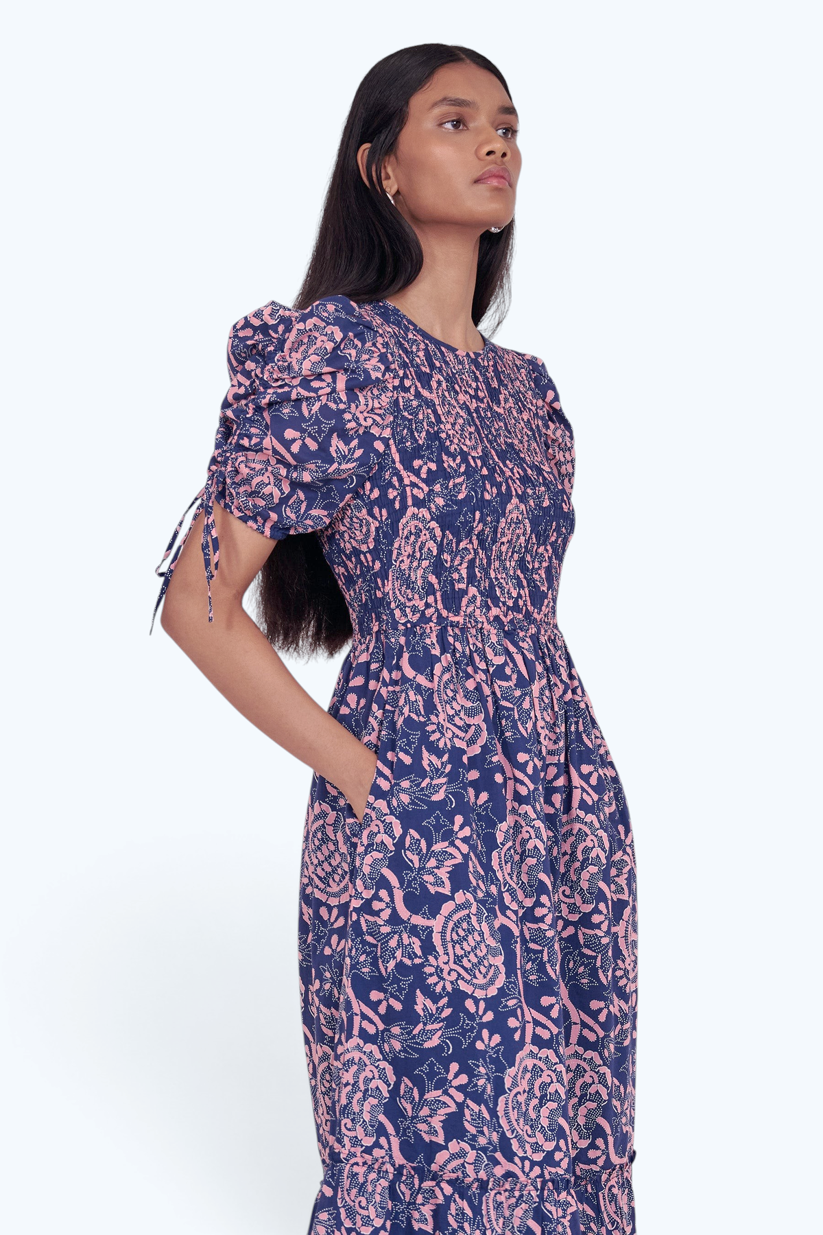 Side view close up of model standing. She is wearing the Queenie midi dress in Coromandel print, featuring a smocked bodice, adjustable drawstring sleeves, and a full lined skirt with pockets.