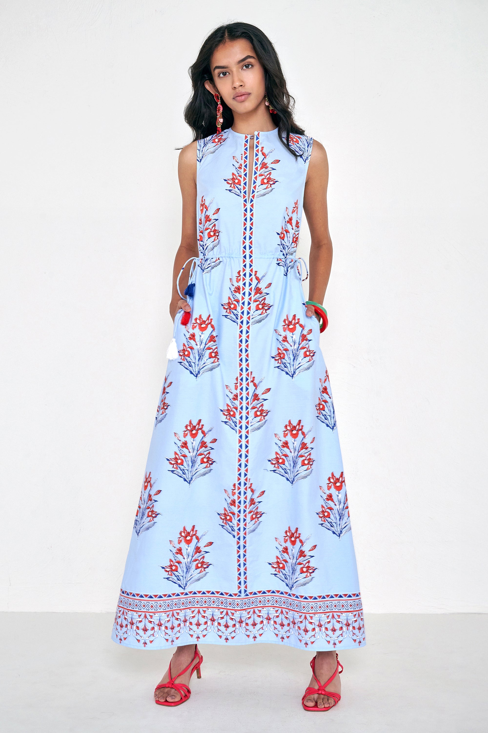 Front view of woman standing. She is wearing the Rhonda dress in the Brigitte print, featuring a sleek column silhouette, side drawstring details with fringe accents, a keyhole neckline, and iris floral motifs.