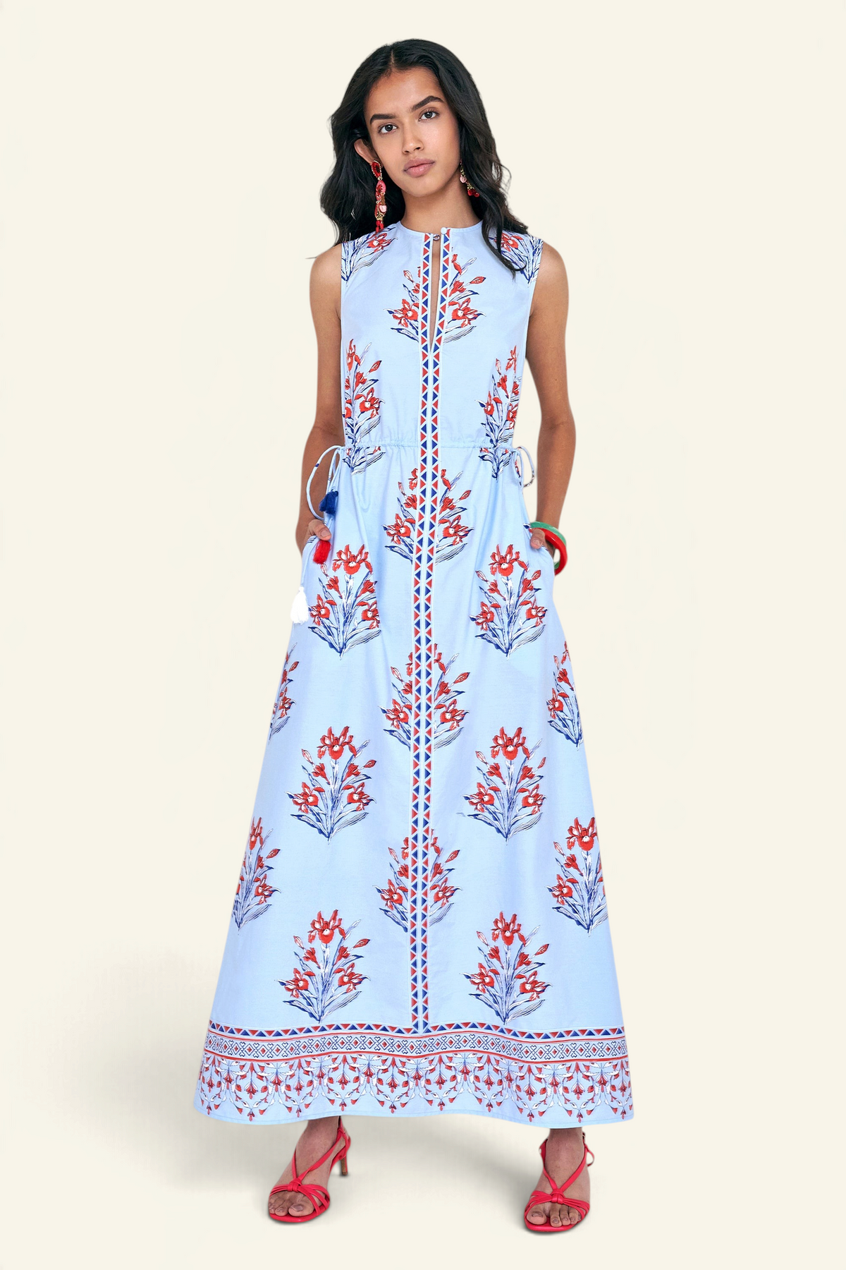 Front view of woman standing. She is wearing the Rhonda dress in the Brigitte print, featuring a sleek column silhouette, side drawstring details with fringe accents, a keyhole neckline, and iris floral motifs.
