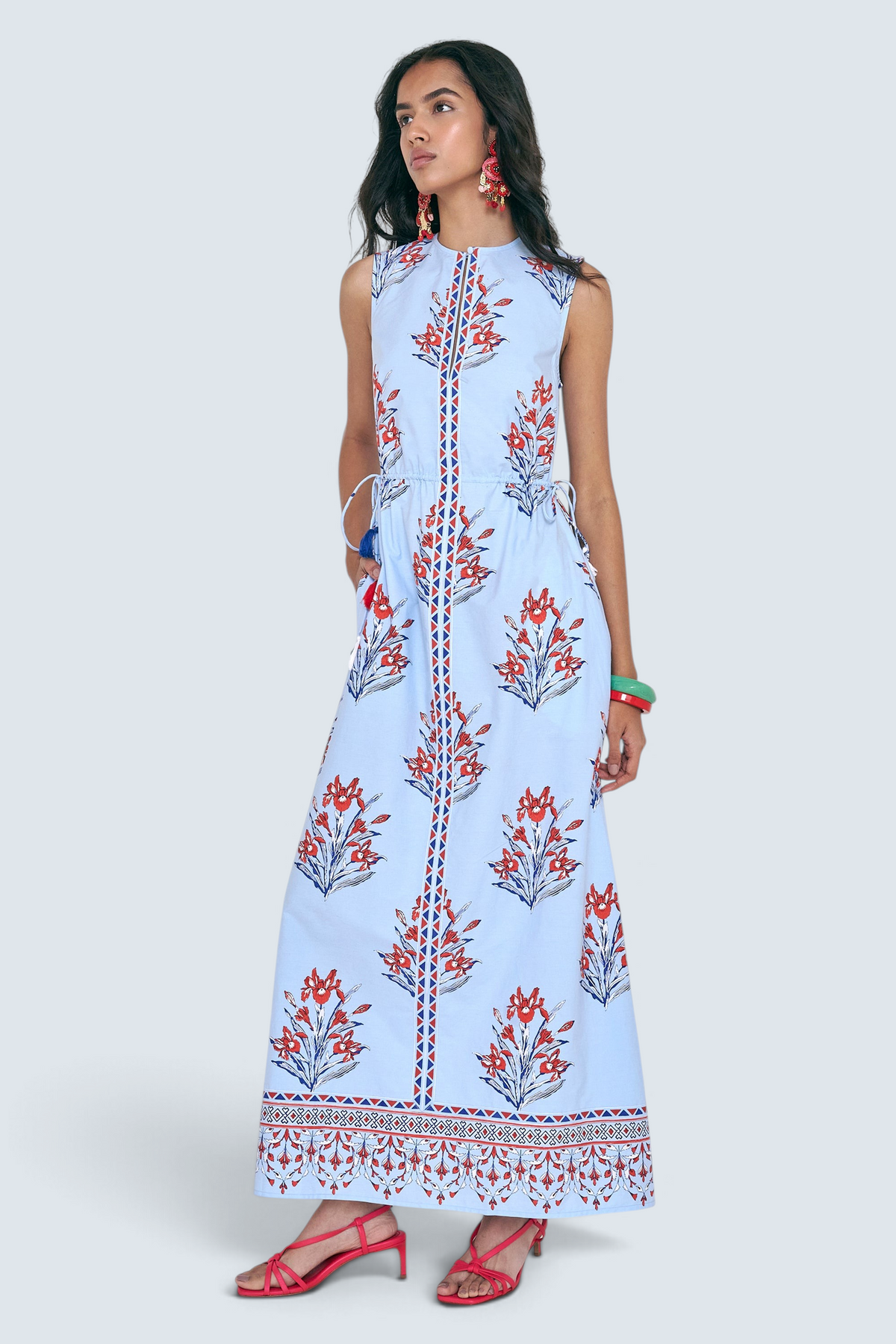 Side view of woman standing. She is wearing the Rhonda dress in the Brigitte print, featuring a sleek column silhouette, side drawstring details with fringe accents, a keyhole neckline, and iris floral motifs.