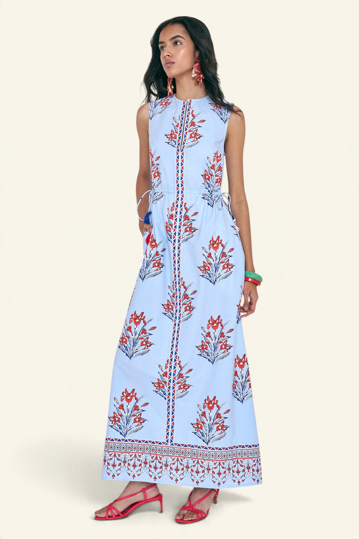 Side view of woman standing. She is wearing the Rhonda dress in the Brigitte print, featuring a sleek column silhouette, side drawstring details with fringe accents, a keyhole neckline, and iris floral motifs.