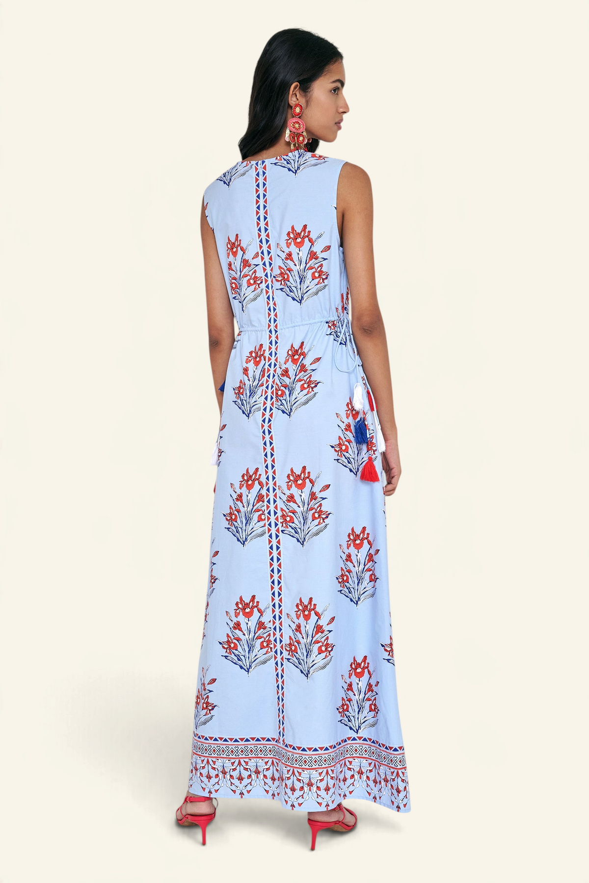 Back view of woman standing. She is wearing the Rhonda dress in the Brigitte print, featuring a sleek column silhouette, side drawstring details with fringe accents, a keyhole neckline, and iris floral motifs.