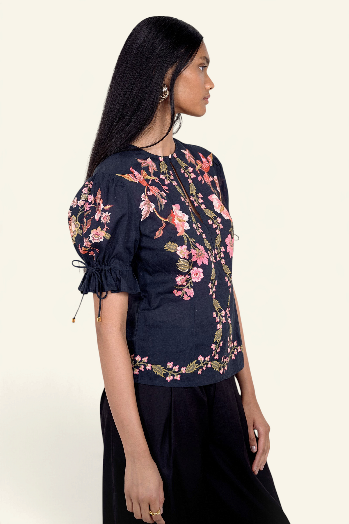 Side view of model standing. She is wearing the Ricki top in Chintz print, featuring a crewneck with keyhole detail, adjustable drawstring sleeves, and vintage-inspired print placement. Its paired with black pants.
