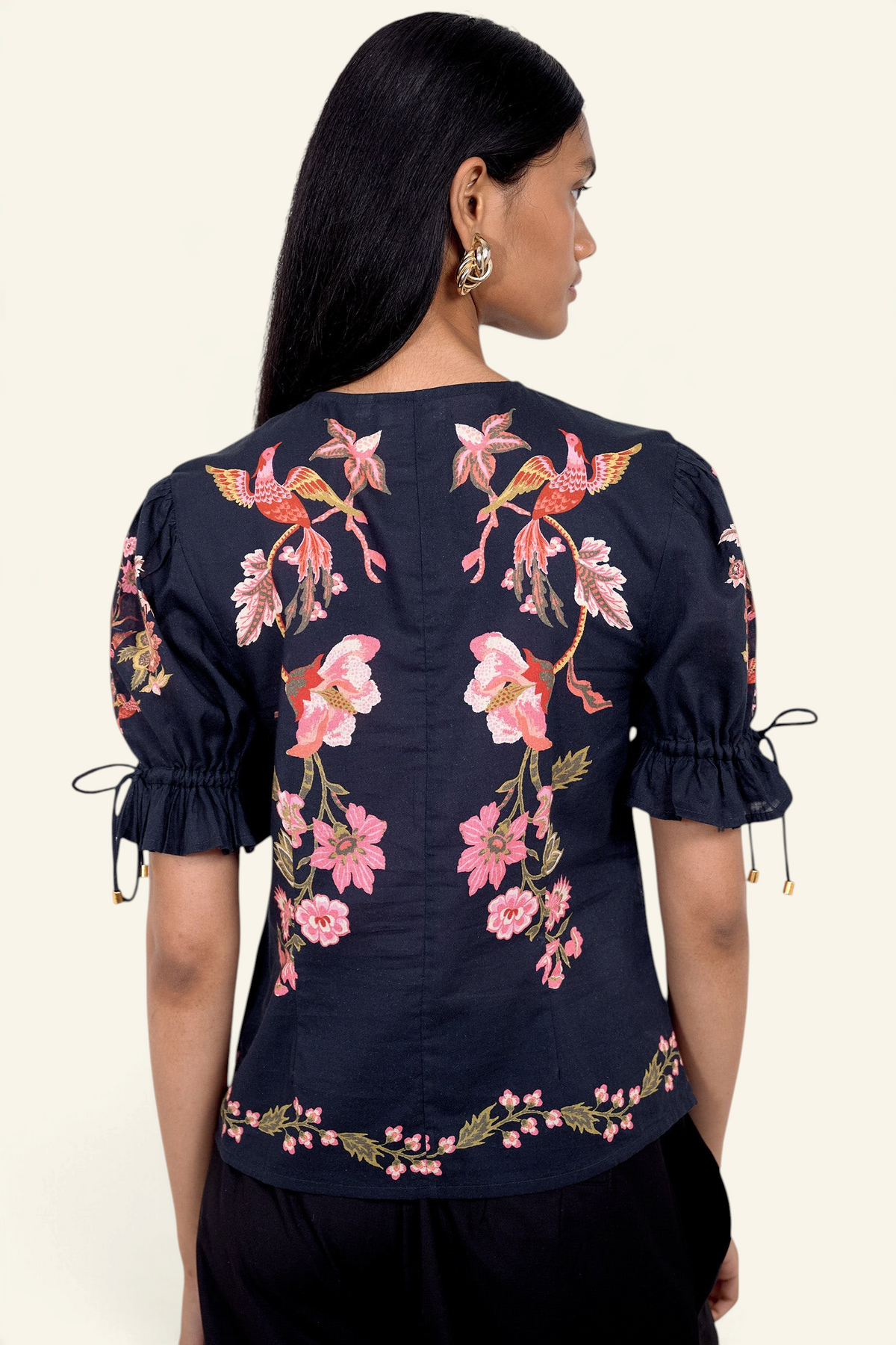 Back view of model standing. She is wearing the Ricki top in Chintz print, featuring a adjustable drawstring sleeves, and vintage-inspired print placement. Its paired with black pants.