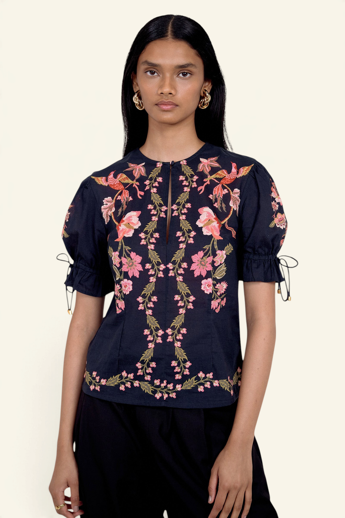 Front view of model standing. She is wearing the Ricki top in Chintz print, featuring a crewneck with keyhole detail, adjustable drawstring sleeves, and vintage-inspired print placement. Its paired with black pants.