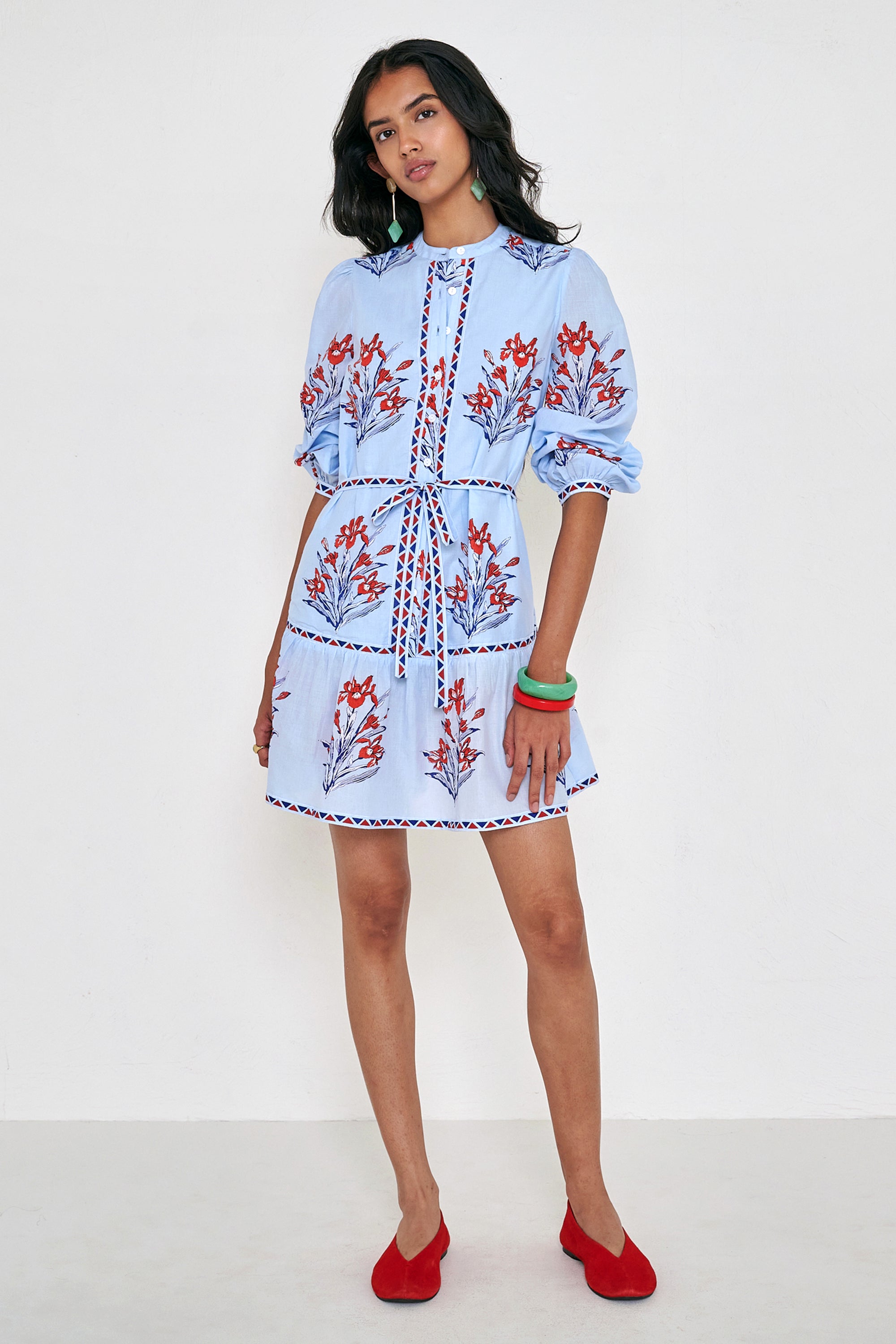 Front view of woman standing. She is wearing the Roma dress in the Brigitte print, featuring a mini shirtdress silhouette, contrast trim details, a detachable belt, and blooming iris floral motifs.