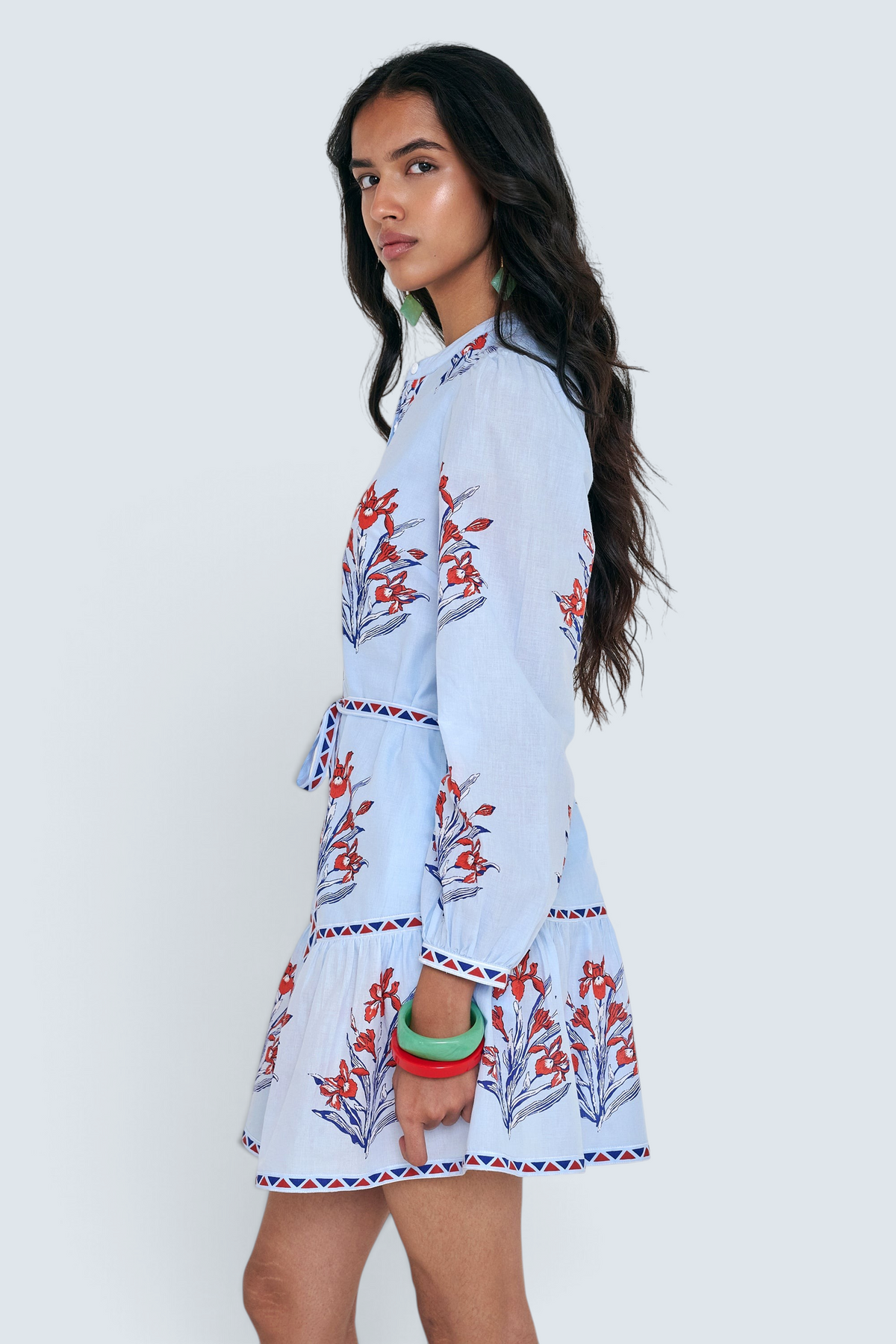 Side view of woman standing. She is wearing the Roma dress in the Brigitte print, featuring a mini shirtdress silhouette, contrast trim details, a detachable belt, and blooming iris floral motifs.