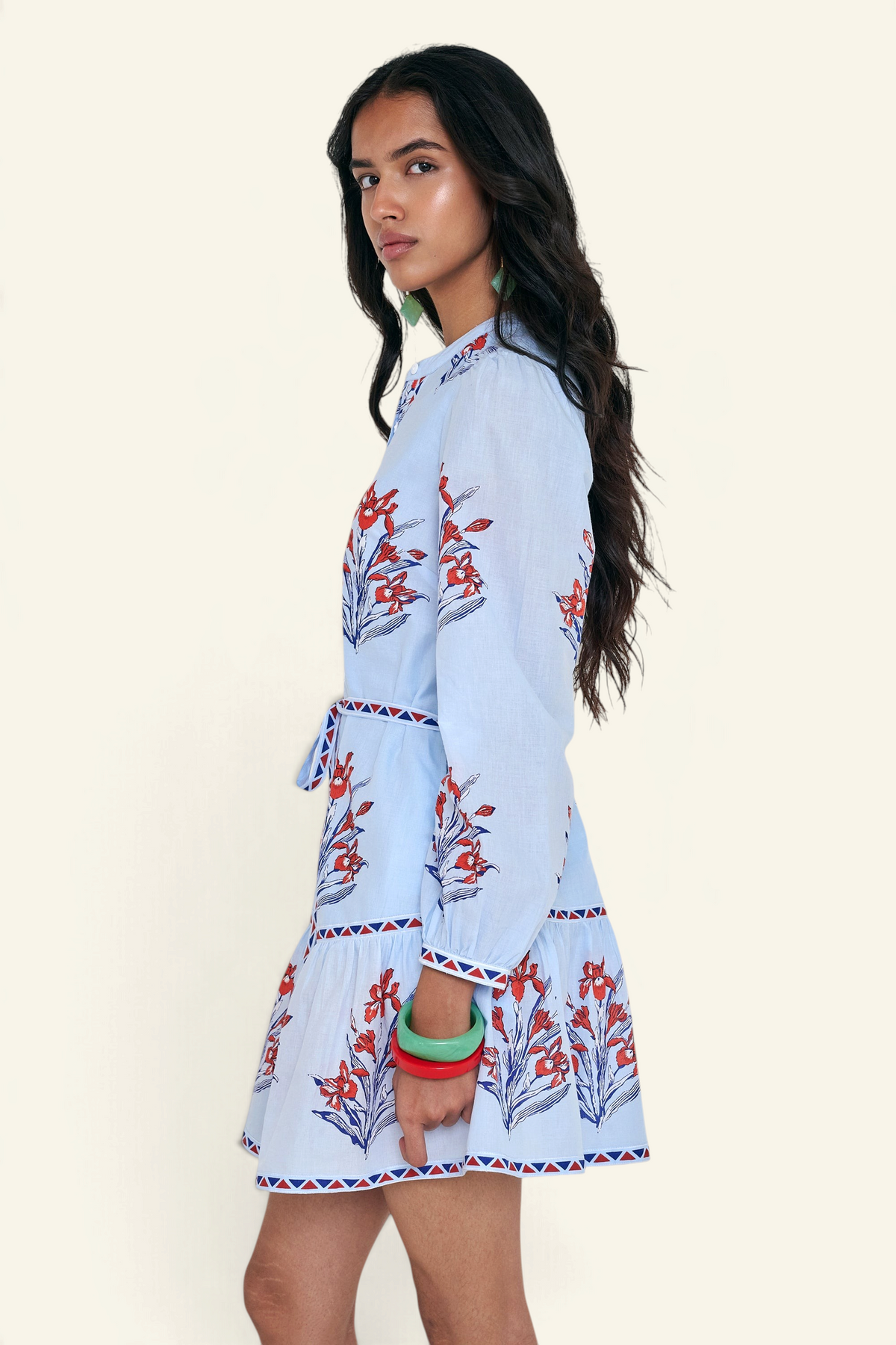 Side view of woman standing. She is wearing the Roma dress in the Brigitte print, featuring a mini shirtdress silhouette, contrast trim details, a detachable belt, and blooming iris floral motifs.