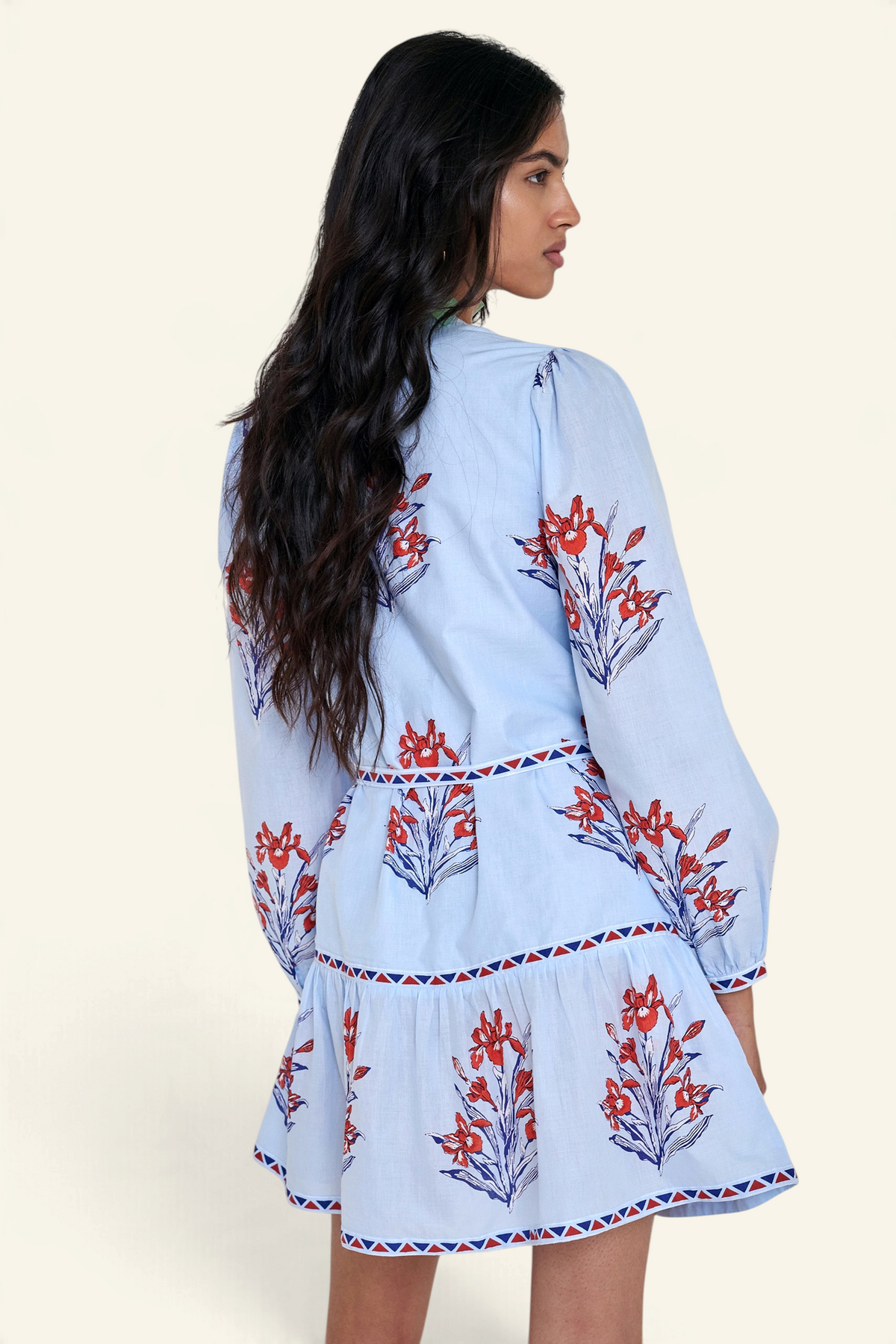 Back view of woman standing. She is wearing the Roma dress in the Brigitte print, featuring a mini shirtdress silhouette, contrast trim details, a detachable belt, and blooming iris floral motifs.