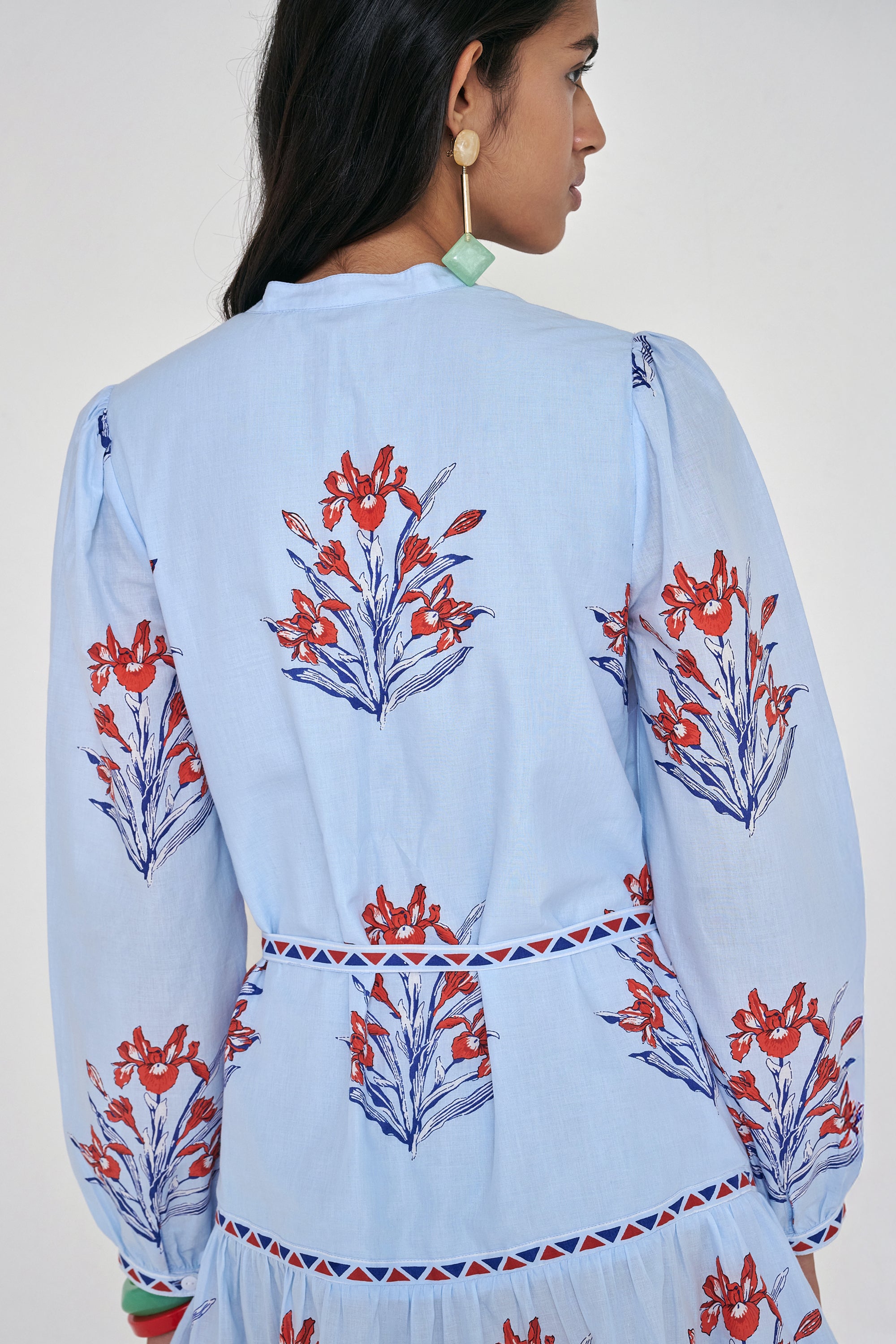 Back view close up of woman standing. She is wearing the Roma dress in the Brigitte print, featuring a mini shirtdress silhouette, contrast trim details, a detachable belt, and blooming iris floral motifs.