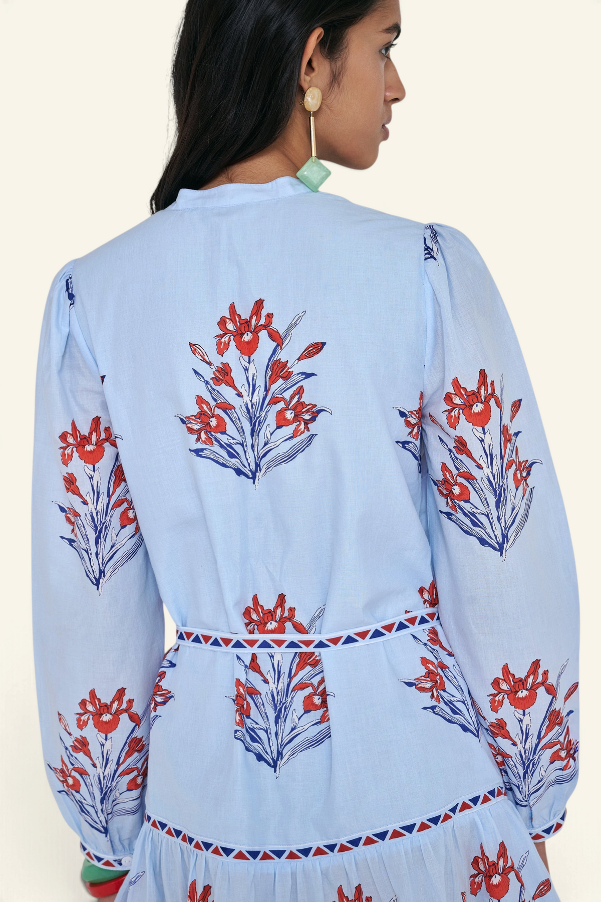 Back view close up of woman standing. She is wearing the Roma dress in the Brigitte print, featuring a mini shirtdress silhouette, contrast trim details, a detachable belt, and blooming iris floral motifs.