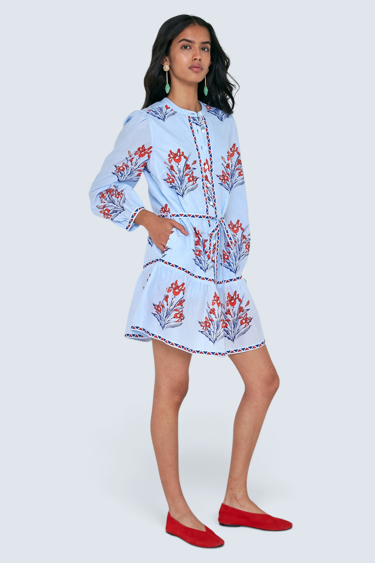 Side view of woman standing. She is wearing the Roma dress in the Brigitte print, featuring a mini shirtdress silhouette, contrast trim details, a detachable belt, and blooming iris floral motifs.
