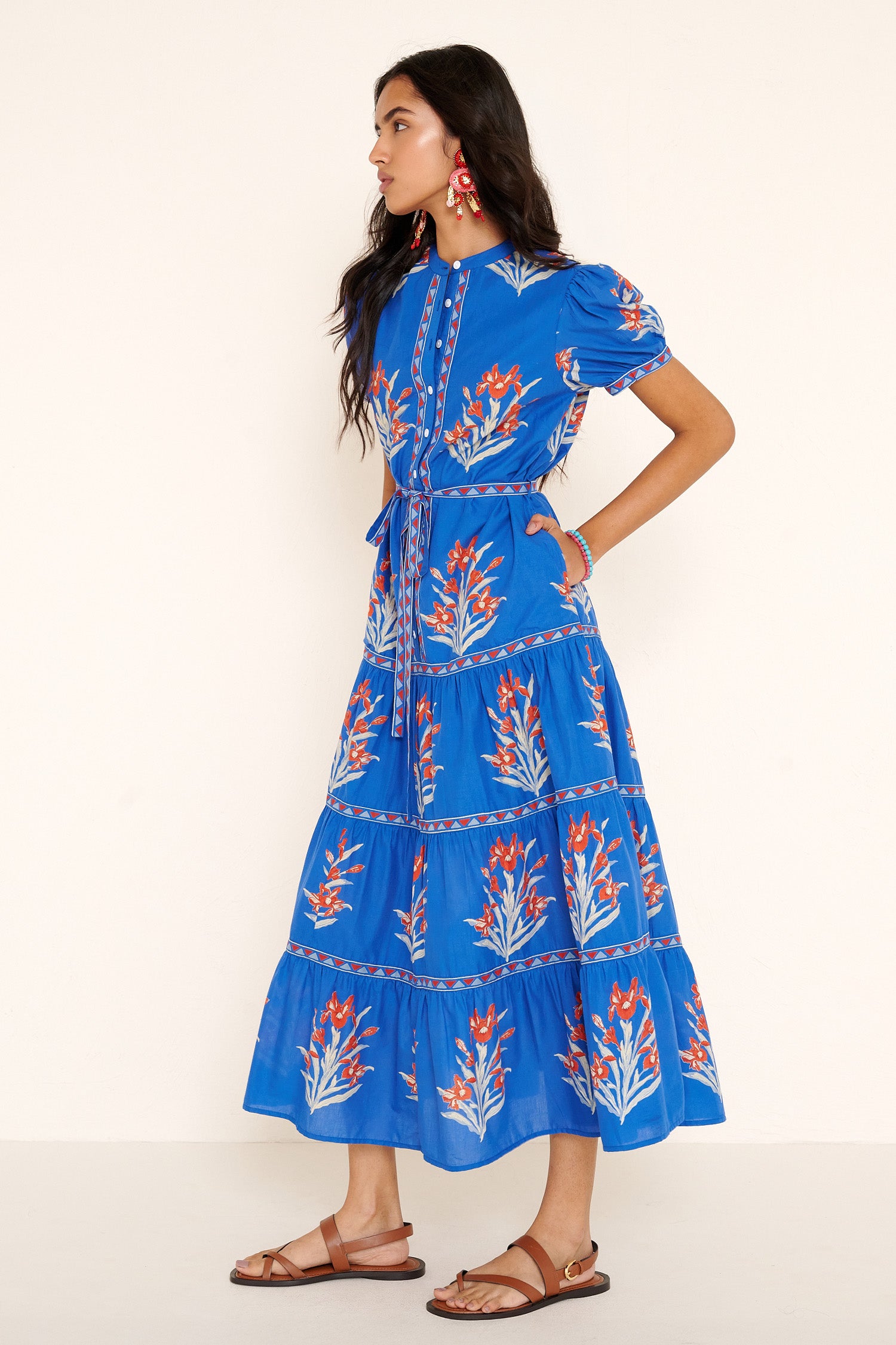 Side view of woman standing. She is wearing the Saylor dress in the Brigitte print, featuring a full-length shirtdress silhouette, tiered skirt, detachable belt, and hand-screen-printed iris floral motifs.