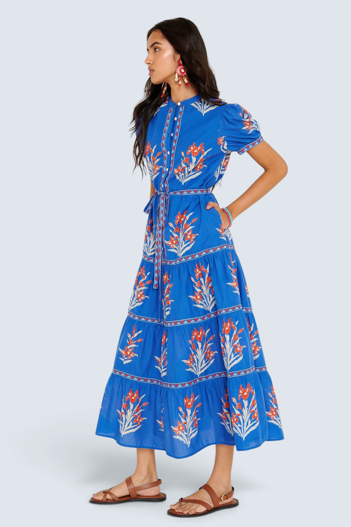 Side view of woman standing. She is wearing the Saylor dress in the Brigitte print, featuring a full-length shirtdress silhouette, tiered skirt, detachable belt, and hand-screen-printed iris floral motifs.