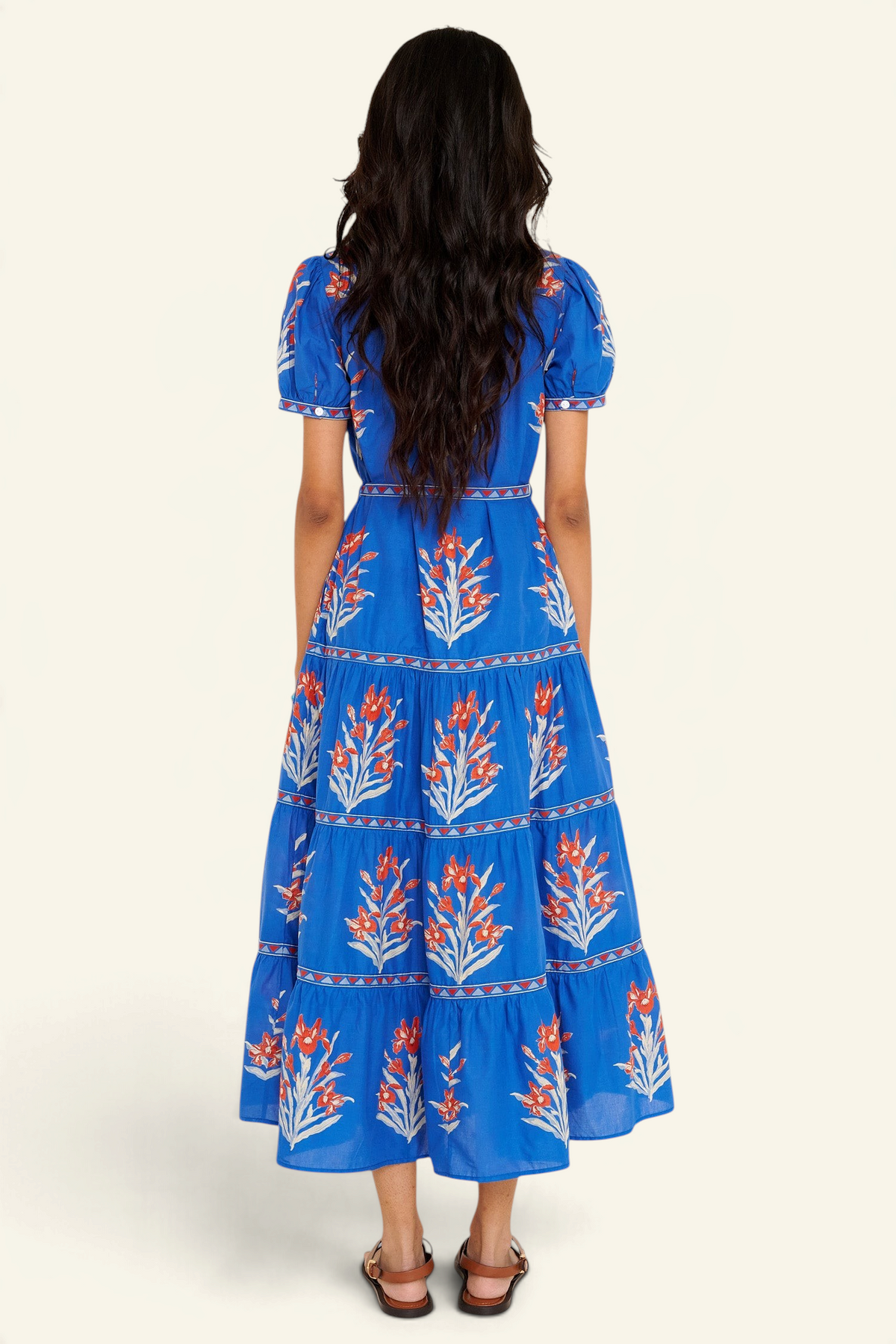 Back view of woman standing. She is wearing the Saylor dress in the Brigitte print, featuring a full-length shirtdress silhouette, tiered skirt, detachable belt, and hand-screen-printed iris floral motifs.