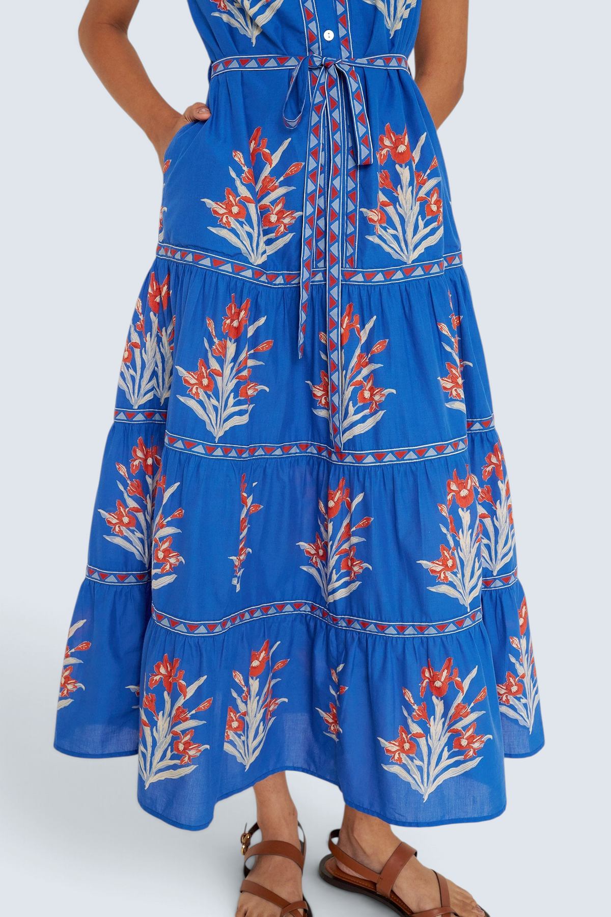Front view close up of woman standing. She is wearing the Saylor dress in the Brigitte print, featuring a full-length shirtdress silhouette, tiered skirt, detachable belt, and hand-screen-printed iris floral motifs.
