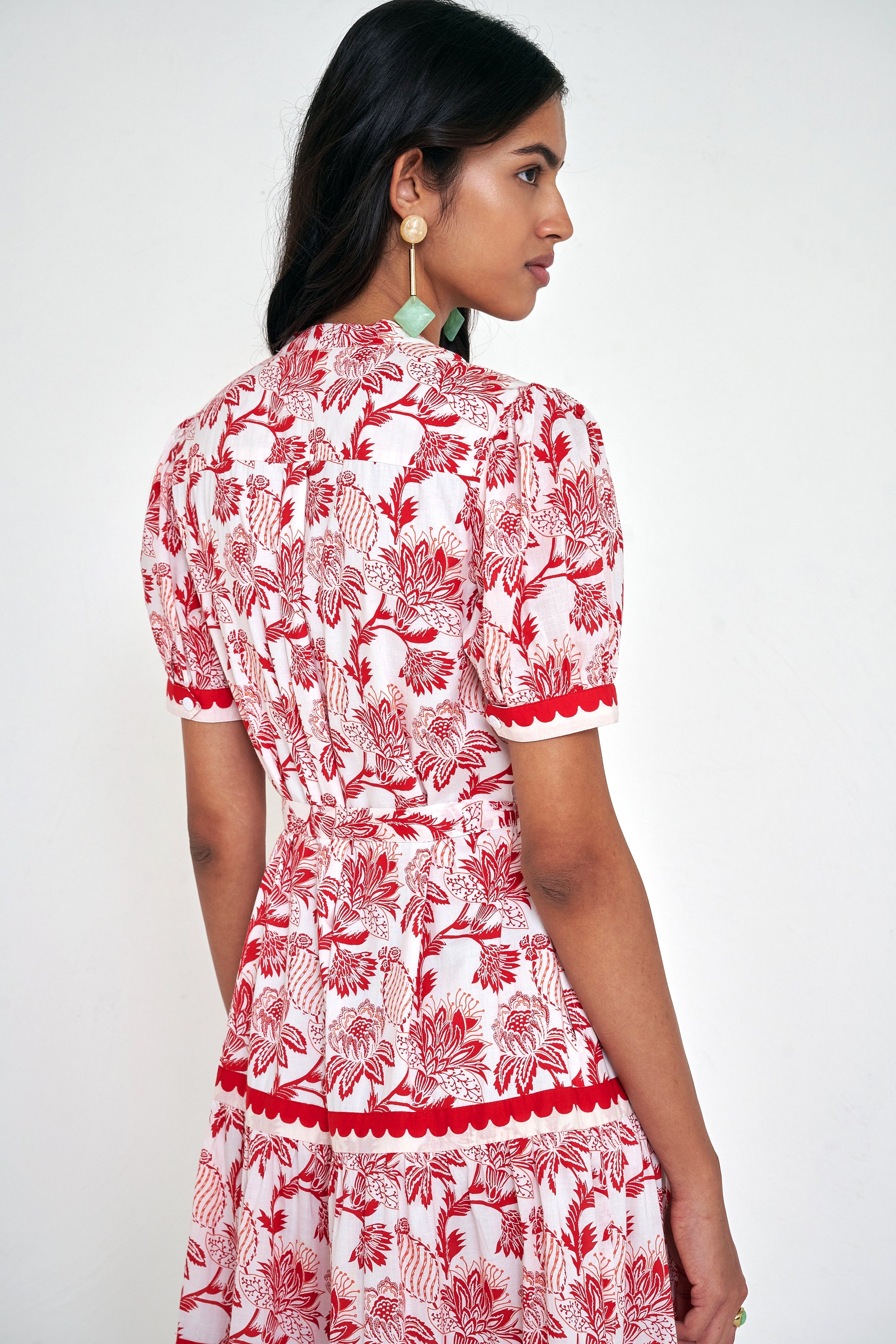 Back view close up of woman standing. She is wearing the Saylor dress in the Lizzie floral print, featuring a full-length shirtdress silhouette, tiered skirt, detachable belt, and winding floral vine motifs.