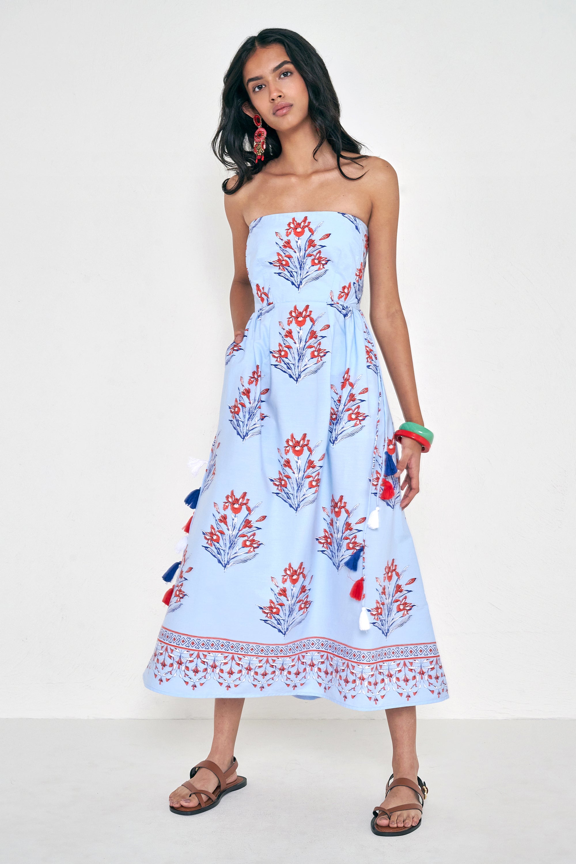 Front view of woman standing. She is wearing the Simona dress in the Brigitte floral print, featuring a strapless bodice, full gathered skirt, and red, white, and blue iris motifs.
